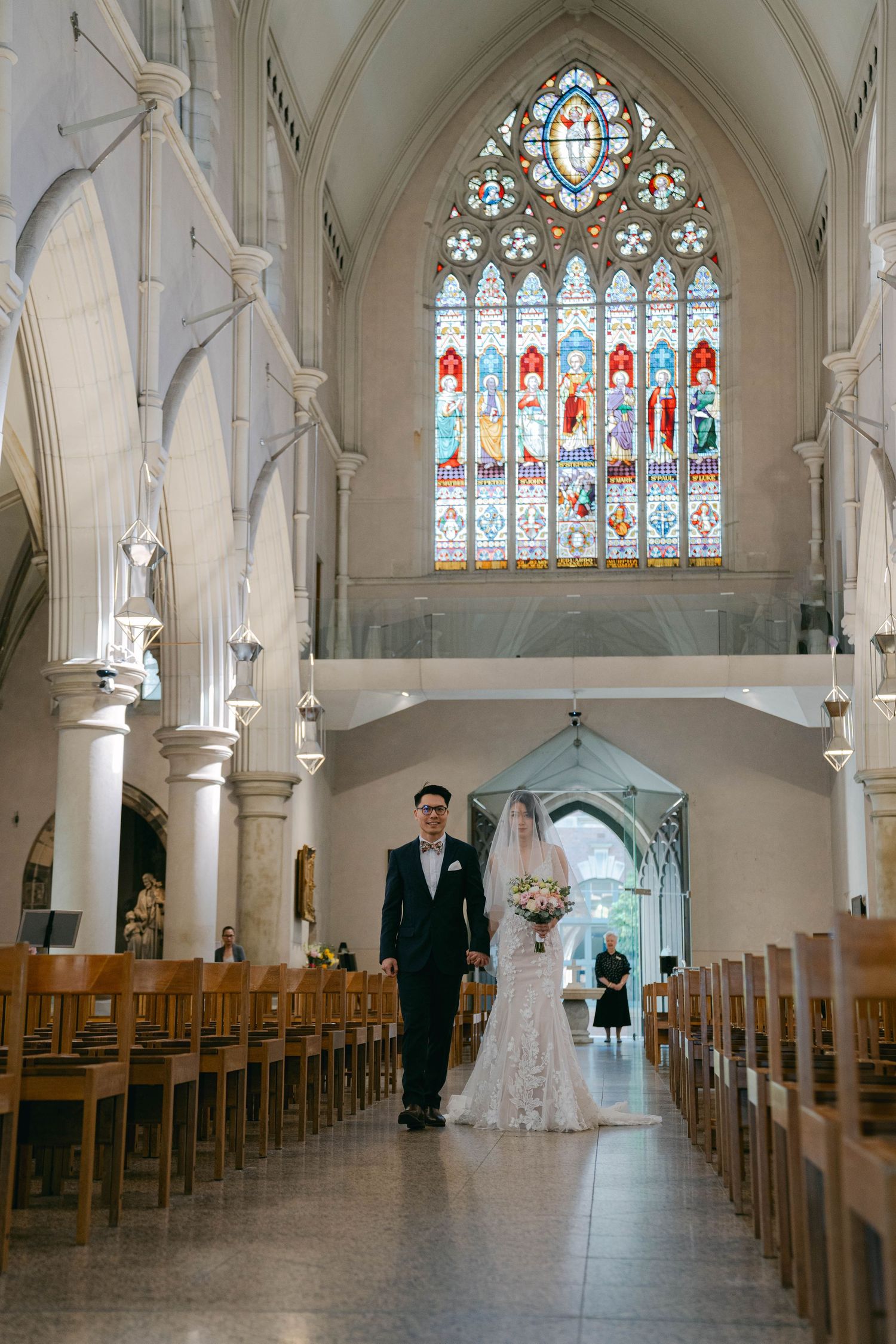 A church interior with wooden pews, stained glass windows and arches shows a wedding ceremony setting.