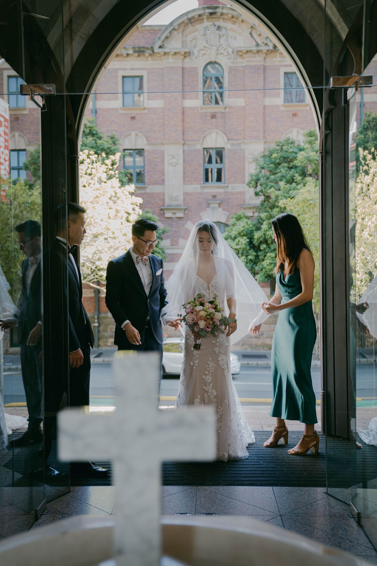 A wedding ceremony taking place through an arched doorway of a church with a blurred cross in the foreground.