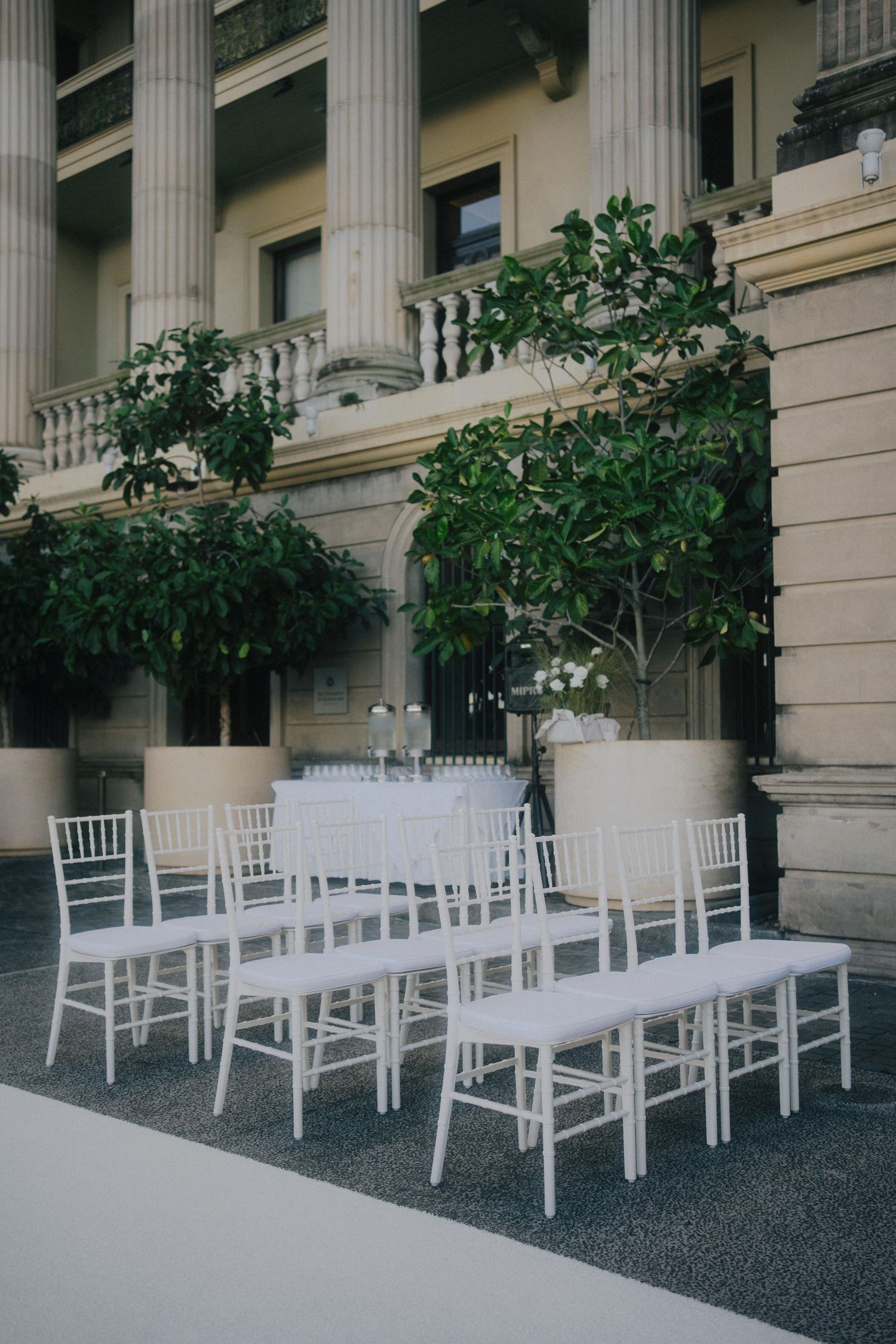 White chiavari chairs arranged for an outdoor ceremony with classical columns and greenery in an elegant venue setting.
