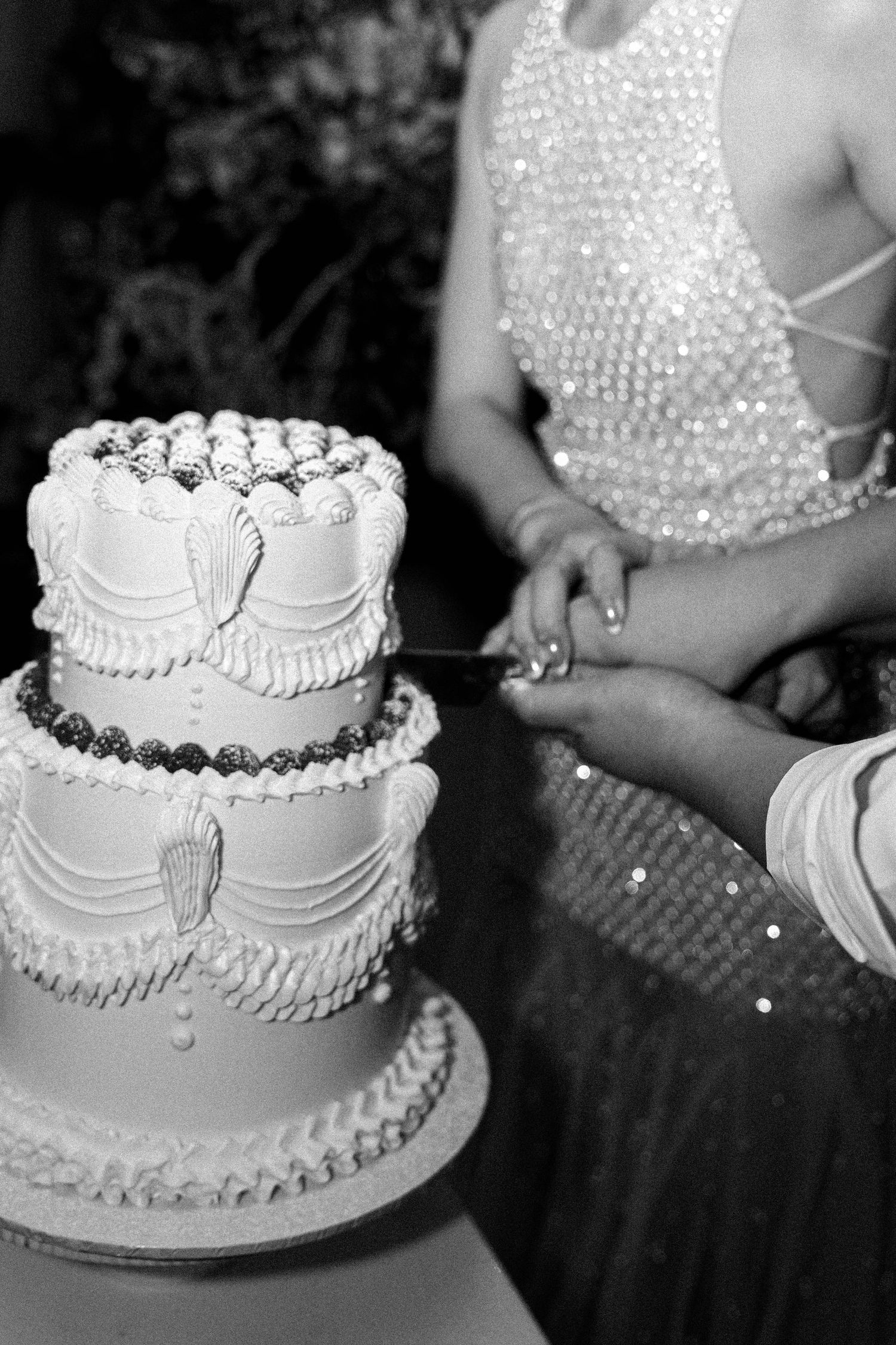 A collage of black and white photos showing close-up views of an elegant white wedding cake with pearl decorations.