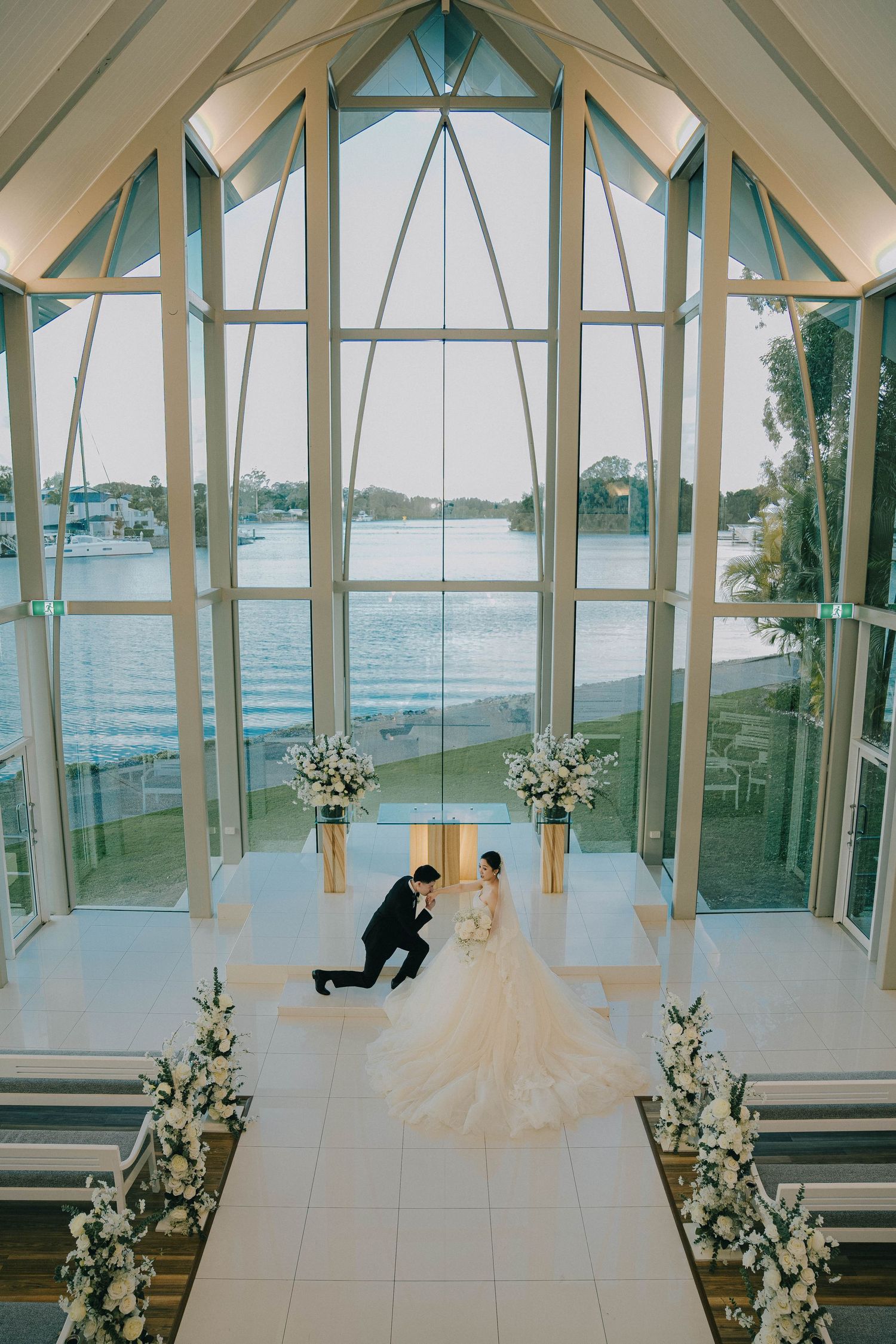 A series of four photos showing a proposal moment in a bright glass-walled chapel overlooking the water.