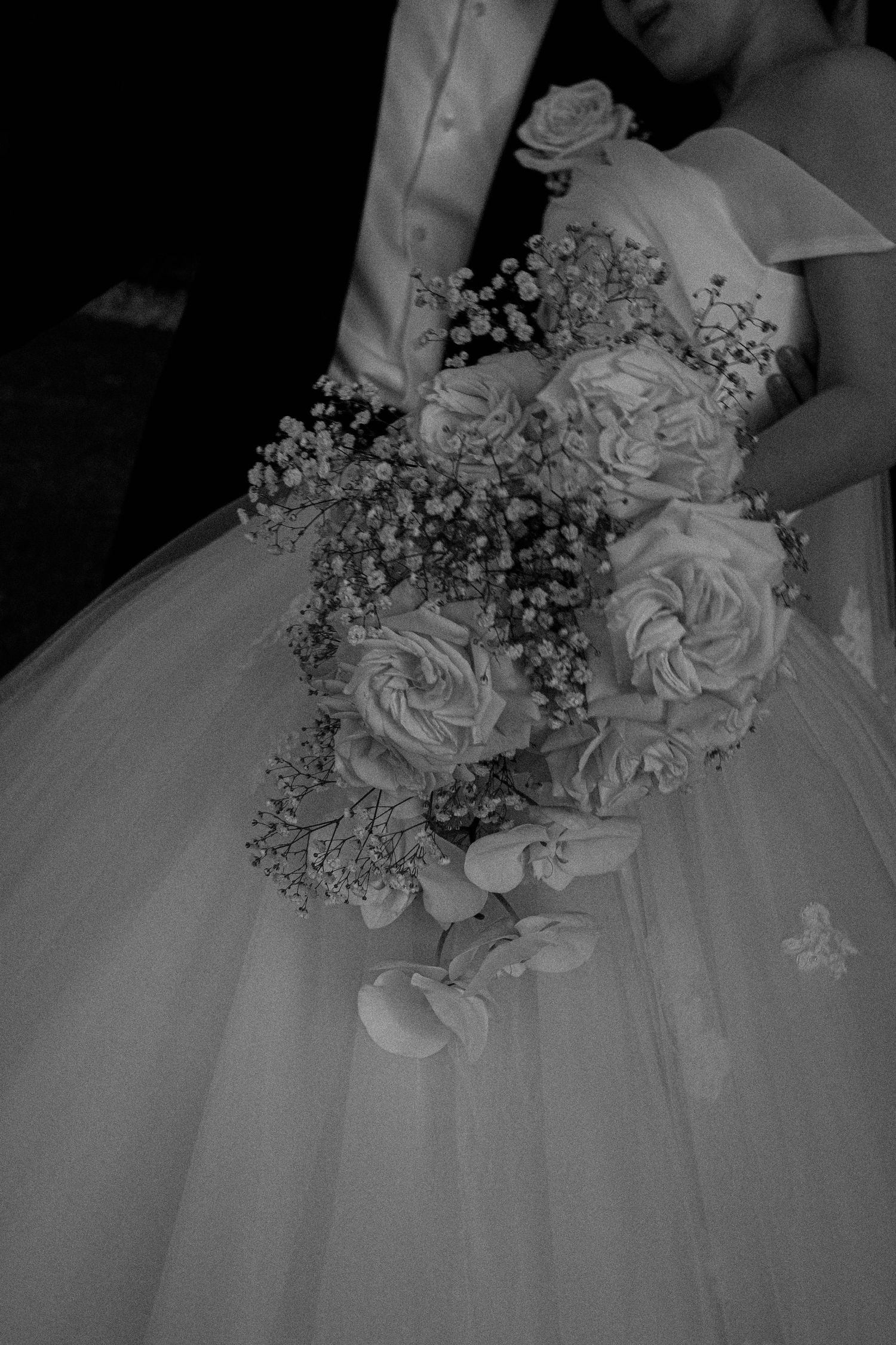 Close-up detail of a white wedding dress with delicate floral bouquet featuring roses and baby's breath in black and white.