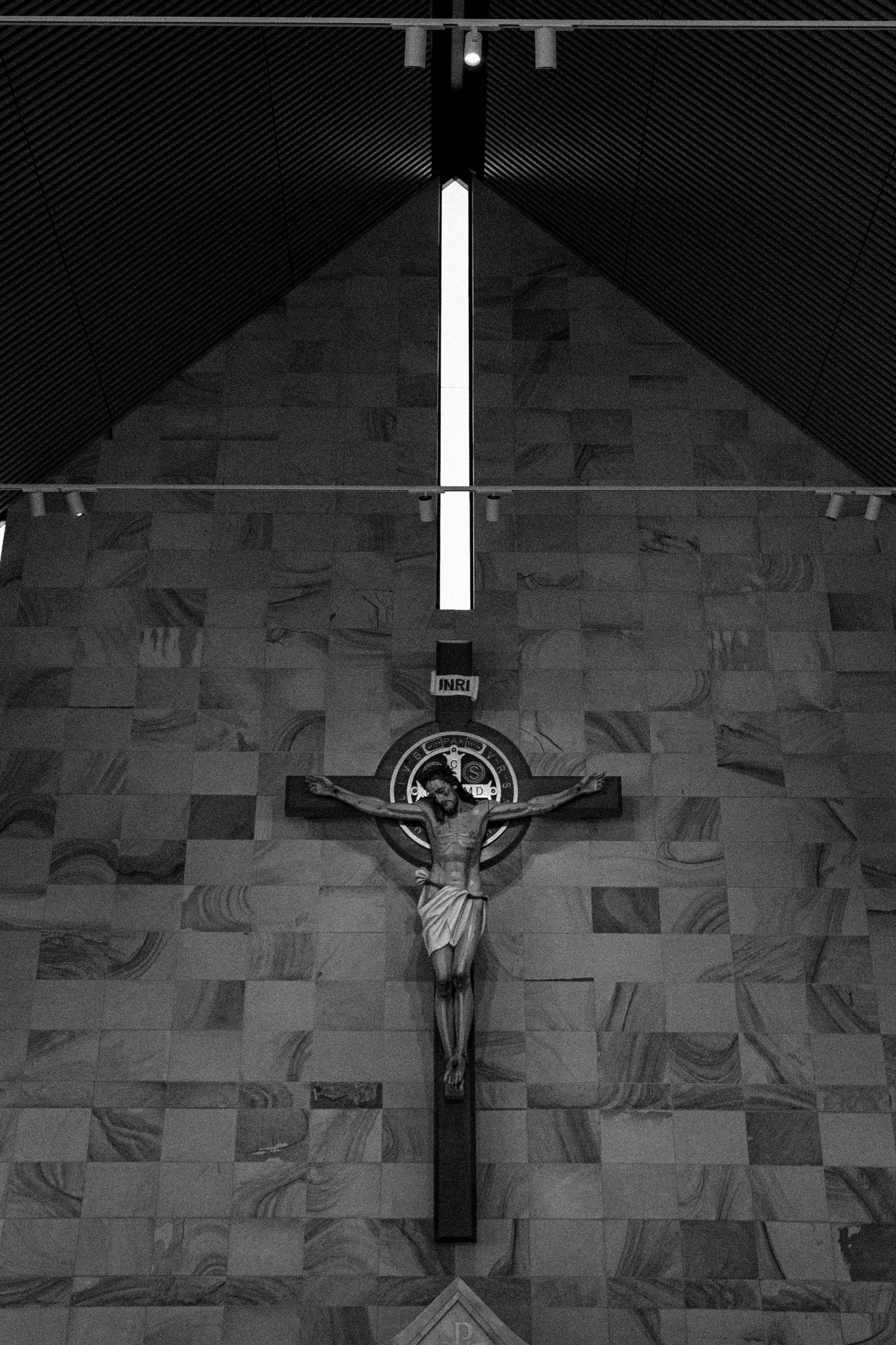 Black and white photo of a crucifix mounted on a stone wall in a church or religious space.