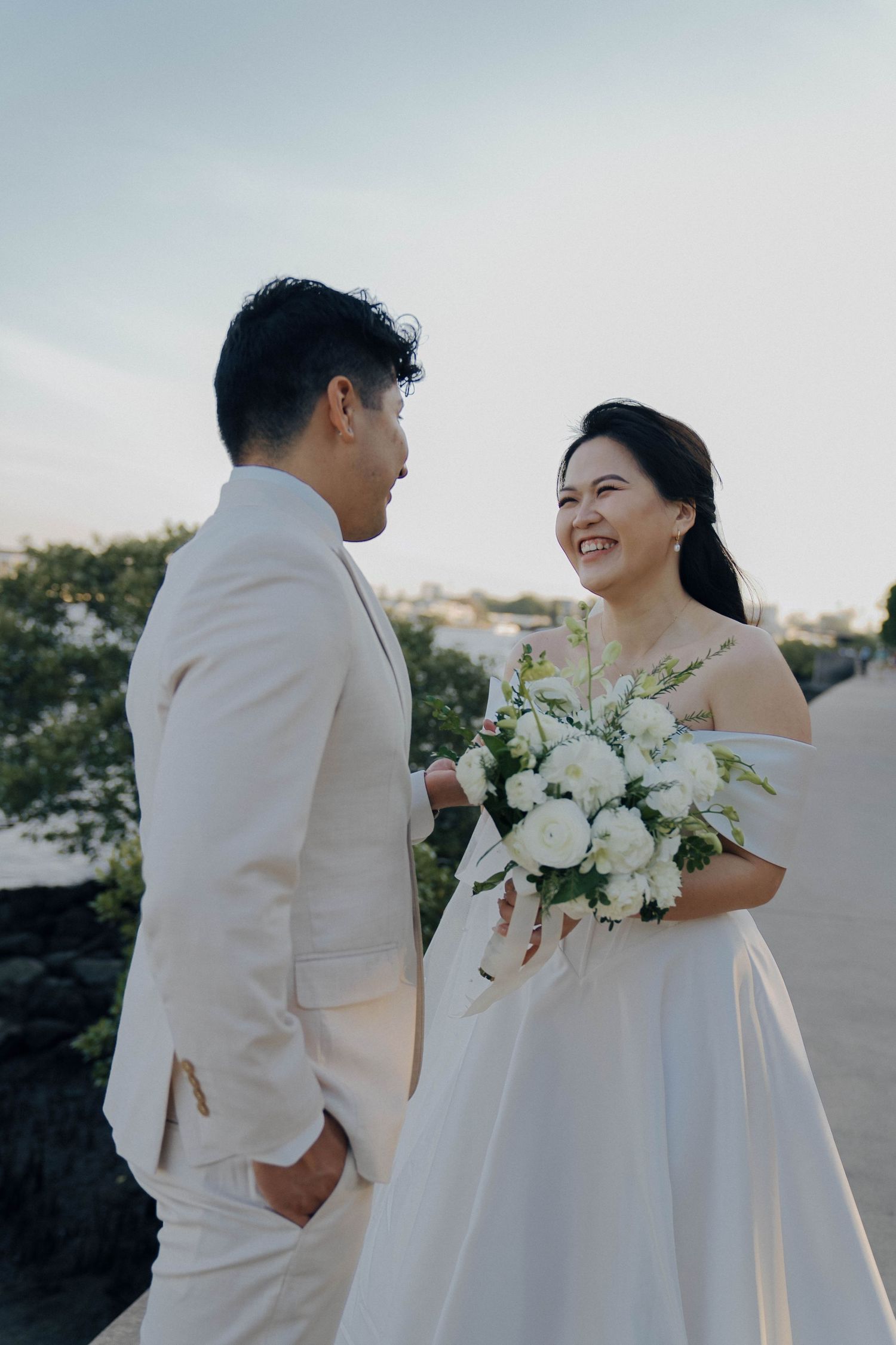 A couple in elegant white wedding attire share intimate moments during their outdoor photo session at sunset.