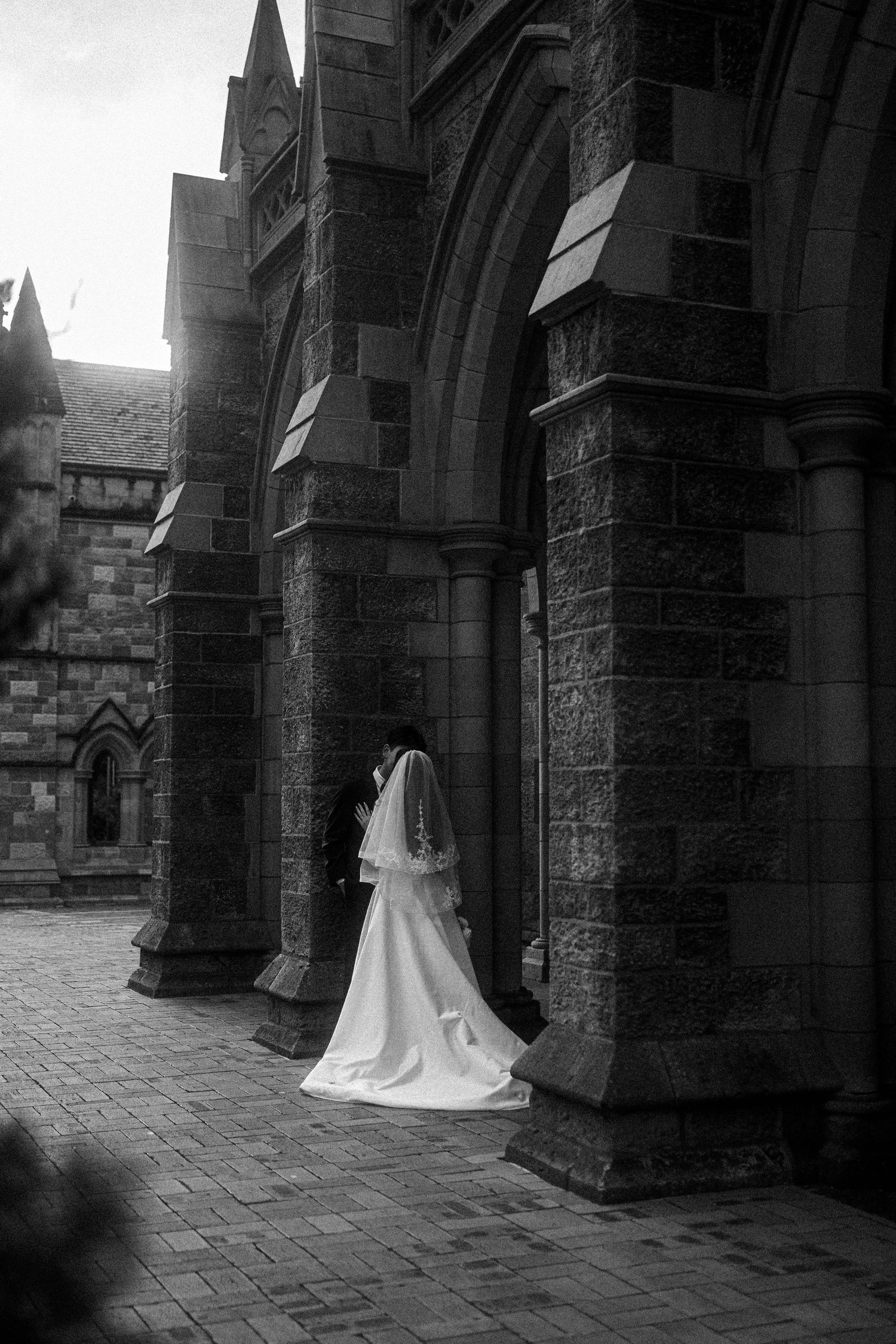 A series of black and white photos showing a flowing wedding dress against stone church archways and pillars.