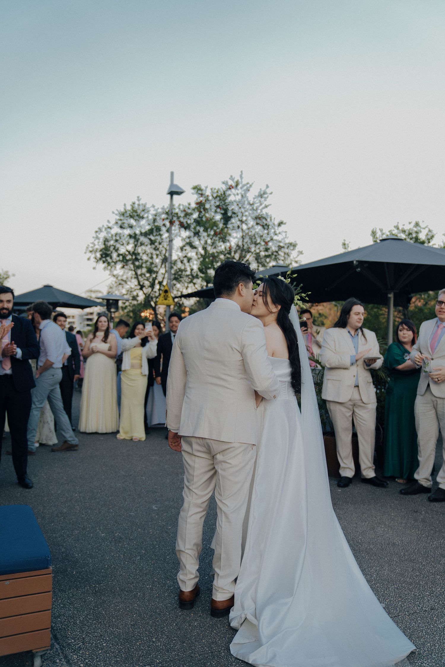 Wedding guests in beige suits and formal attire gather outdoors during a celebration at dusk.