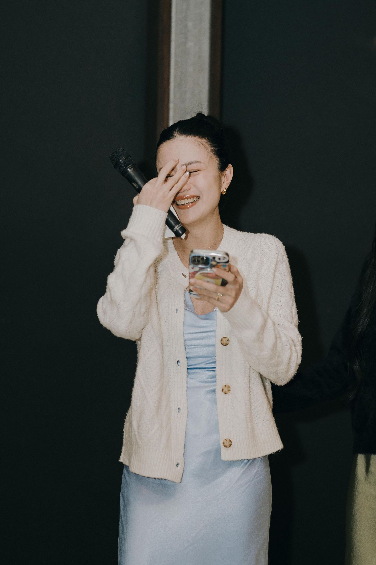 A figure in a cream cardigan and blue top poses playfully in a photo series against a dark background.