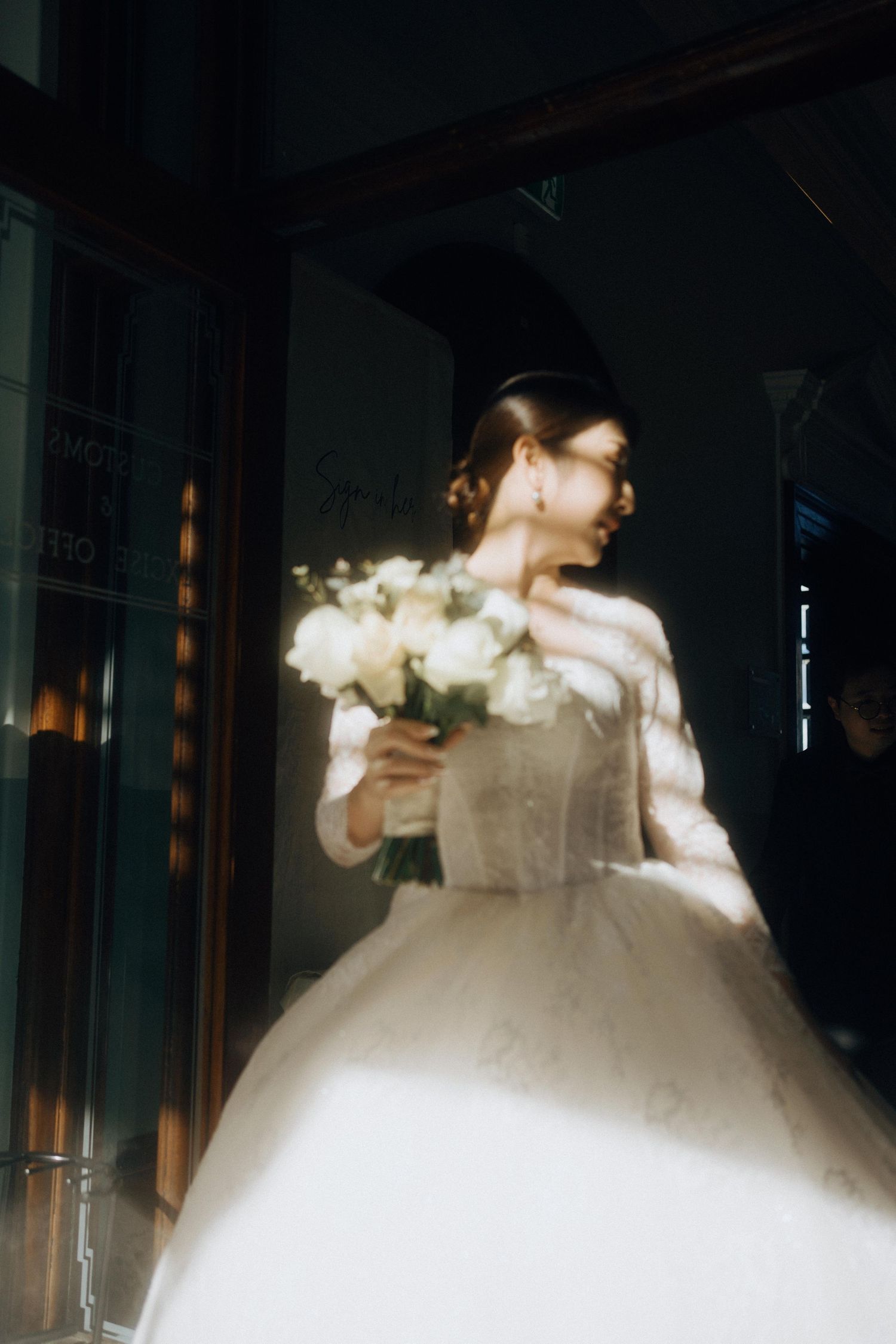A bride in a classic white ballgown holds a bouquet of white flowers in a moody, atmospheric setting.