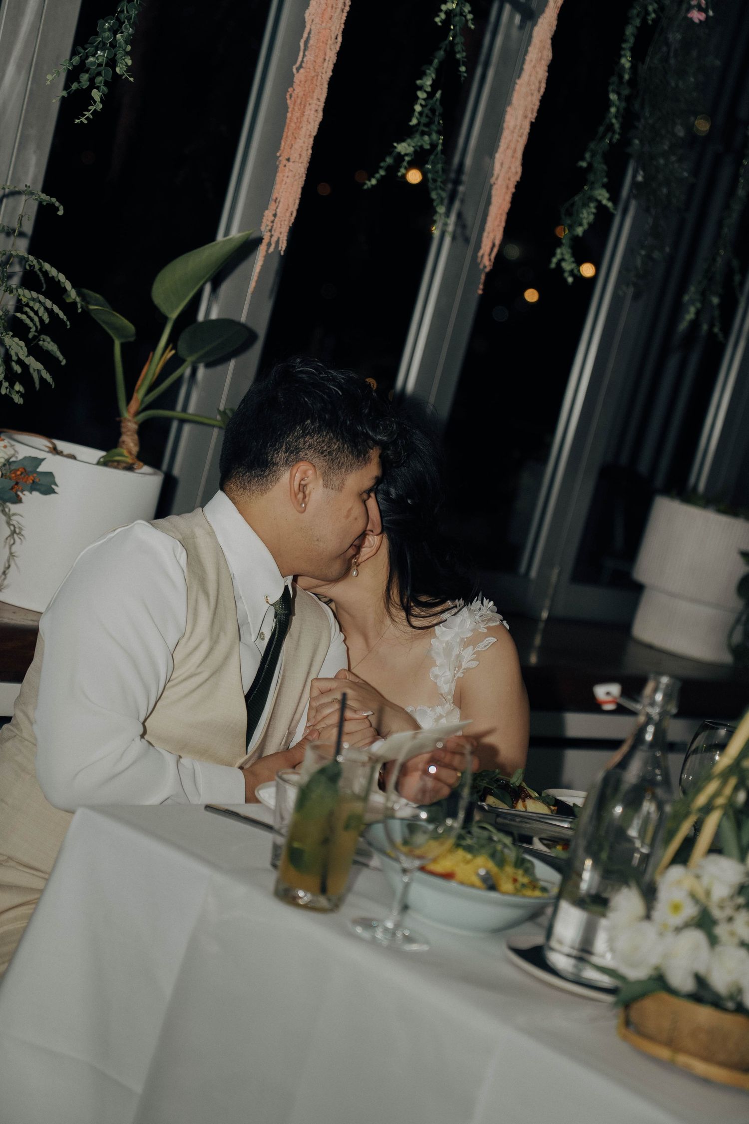 A couple in wedding attire share an intimate moment at an elegant dinner table.