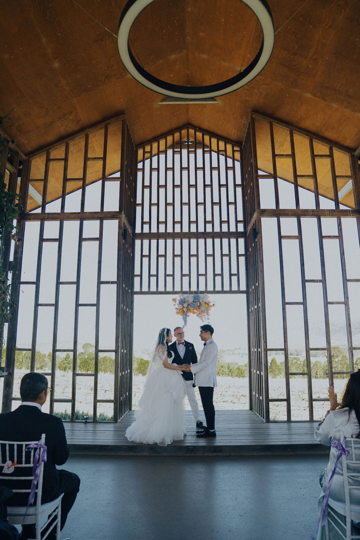Wedding ceremony taking place in a modern chapel with large windows overlooking scenic views.