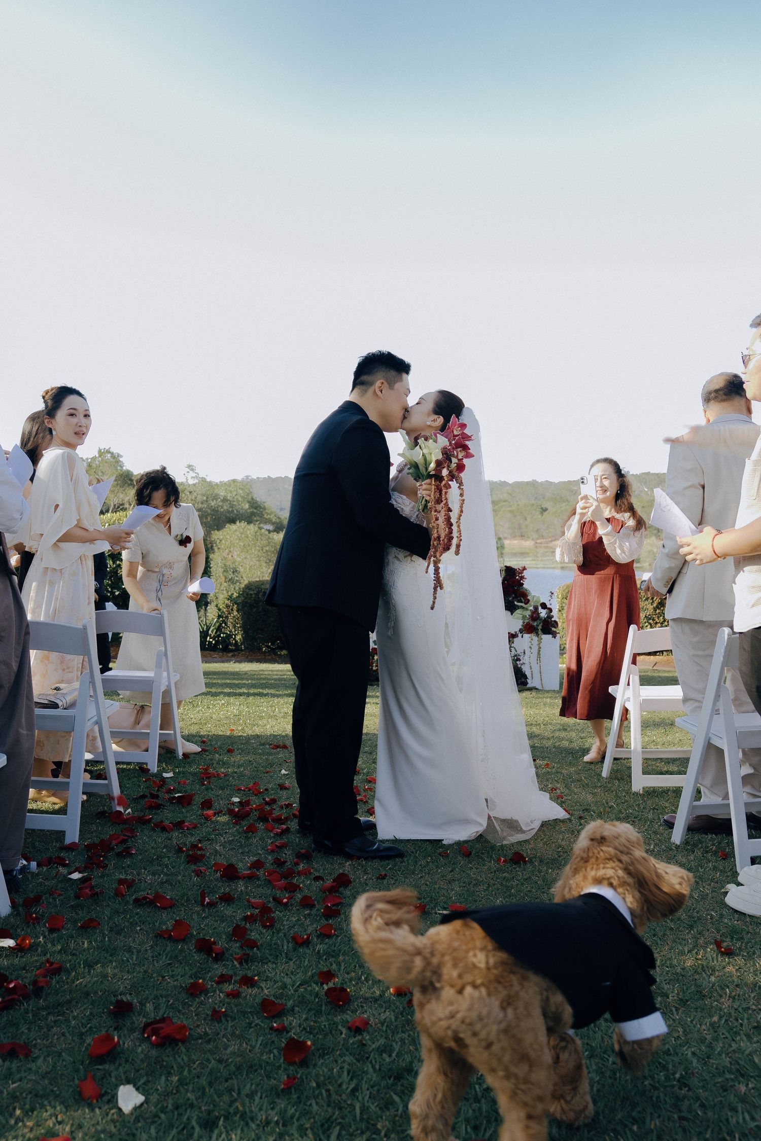 A series of outdoor wedding ceremony photos with guests in white attire and red floral decorations on a grassy field.