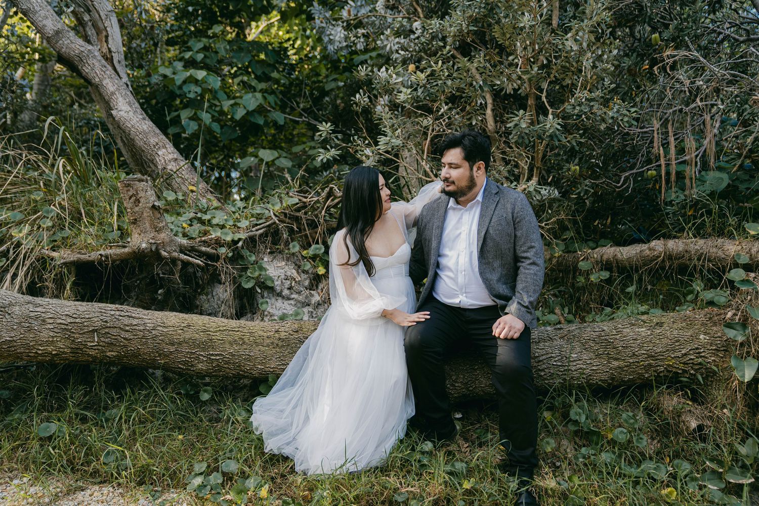 A romantic wedding couple poses in a serene forest setting with fallen trees and natural greenery.