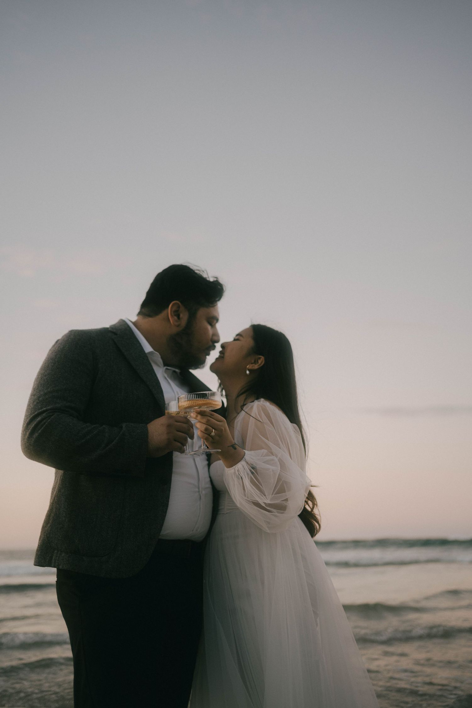 A romantic couple embraces on a moody beach at sunset in a series of intimate photos.