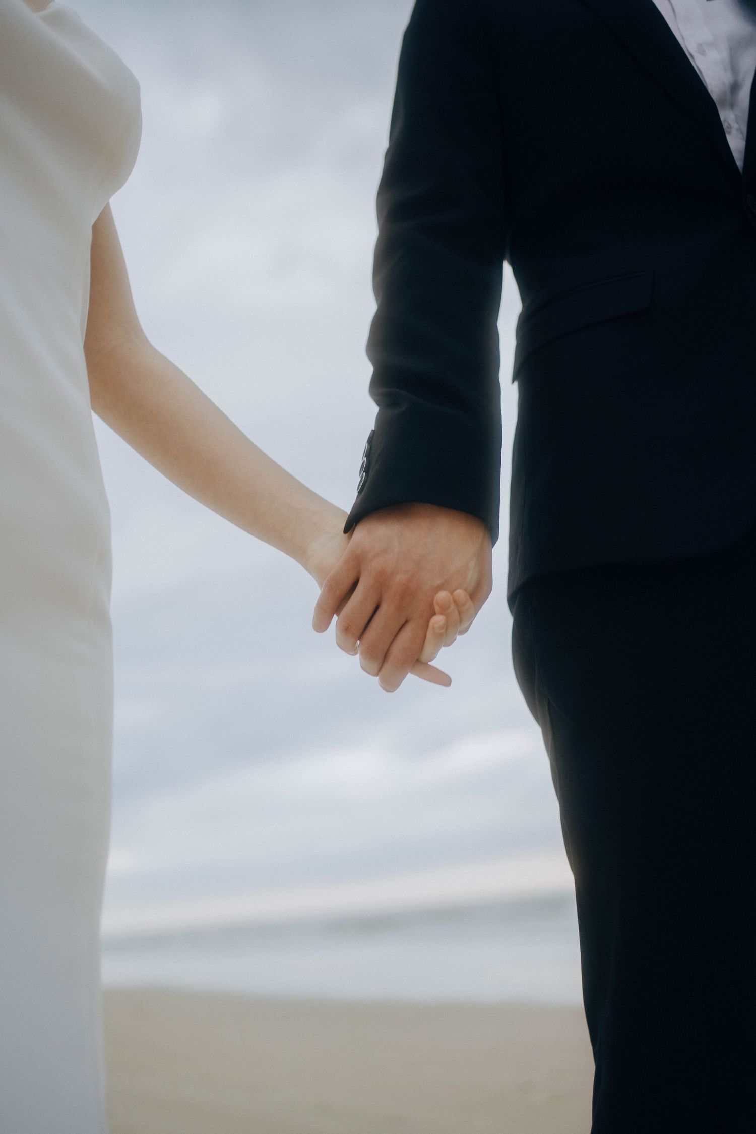 Close-up view of two people holding hands against a cloudy sky background.
