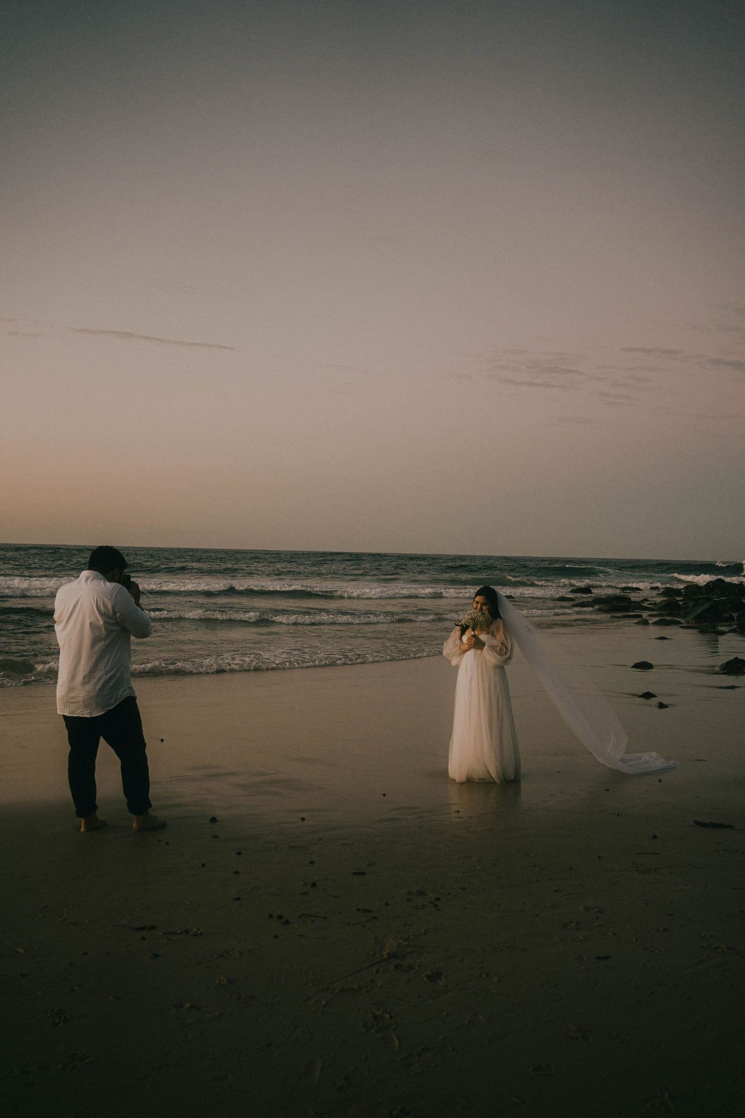 A romantic beach wedding photoshoot at sunset with silhouettes walking along the misty shoreline.