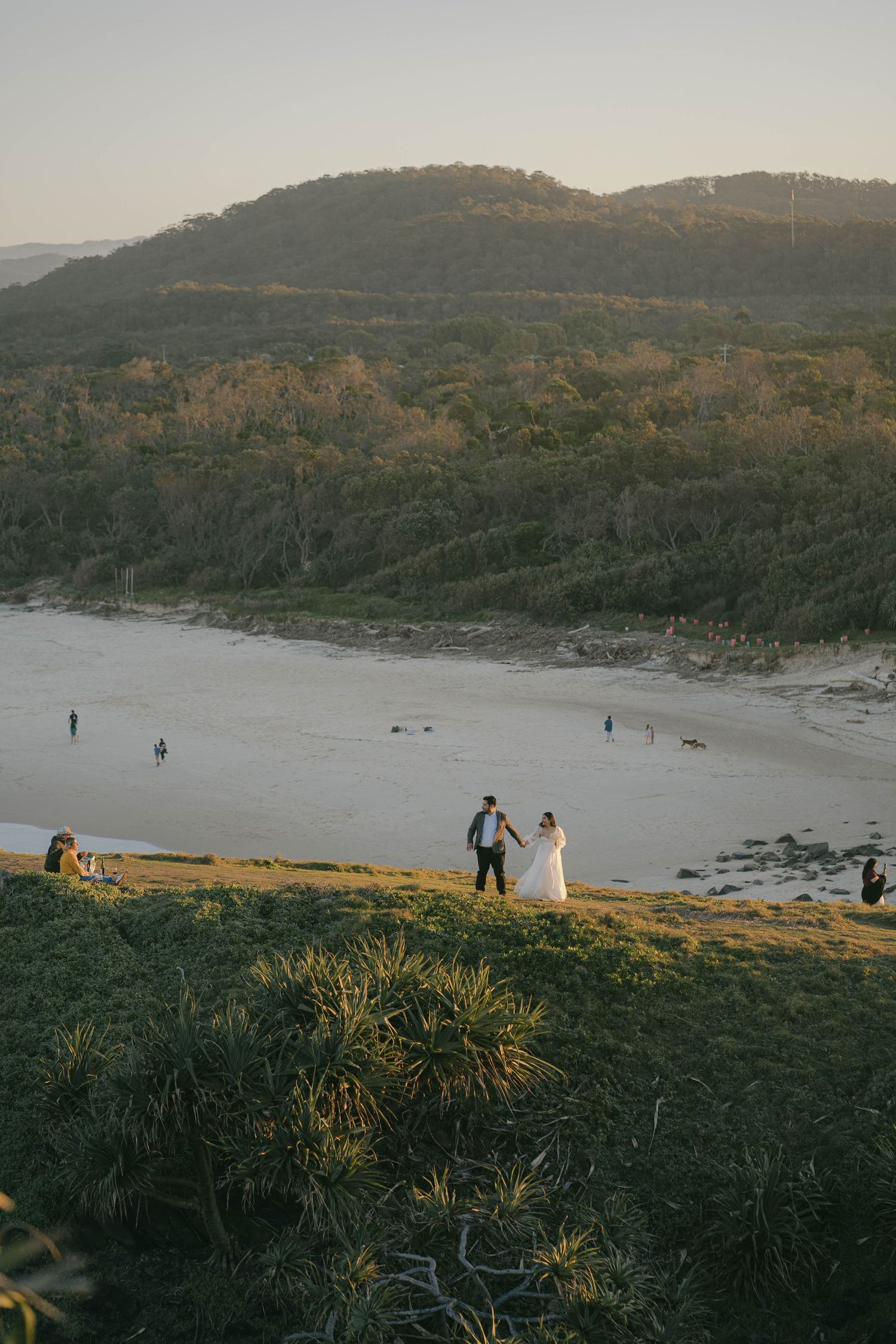 Scenic coastal landscape sequence showing grassy cliffs overlooking a beach at golden hour with distant figures.
