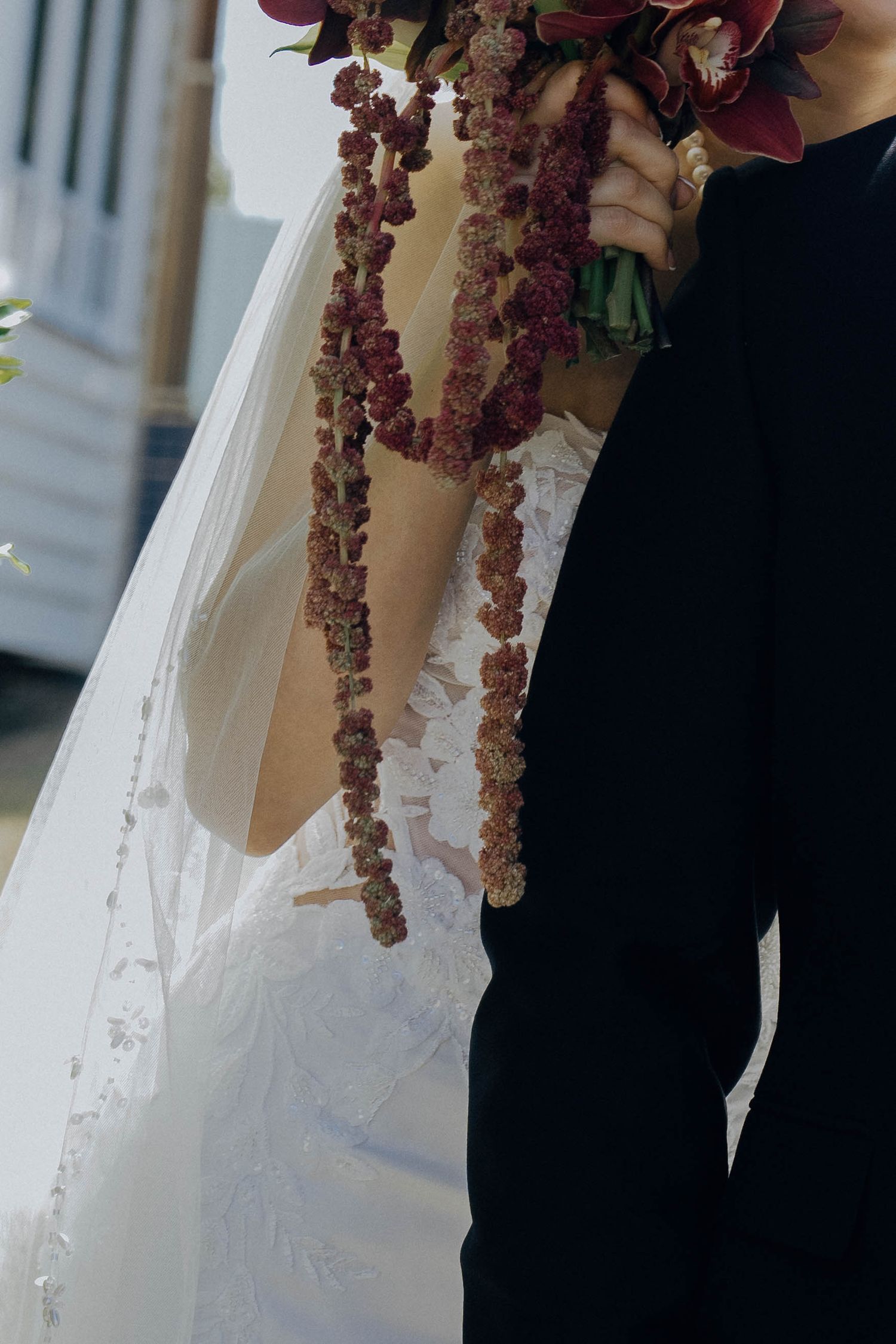 A close-up detail of a wedding dress and black suit with hanging floral lei decorations.