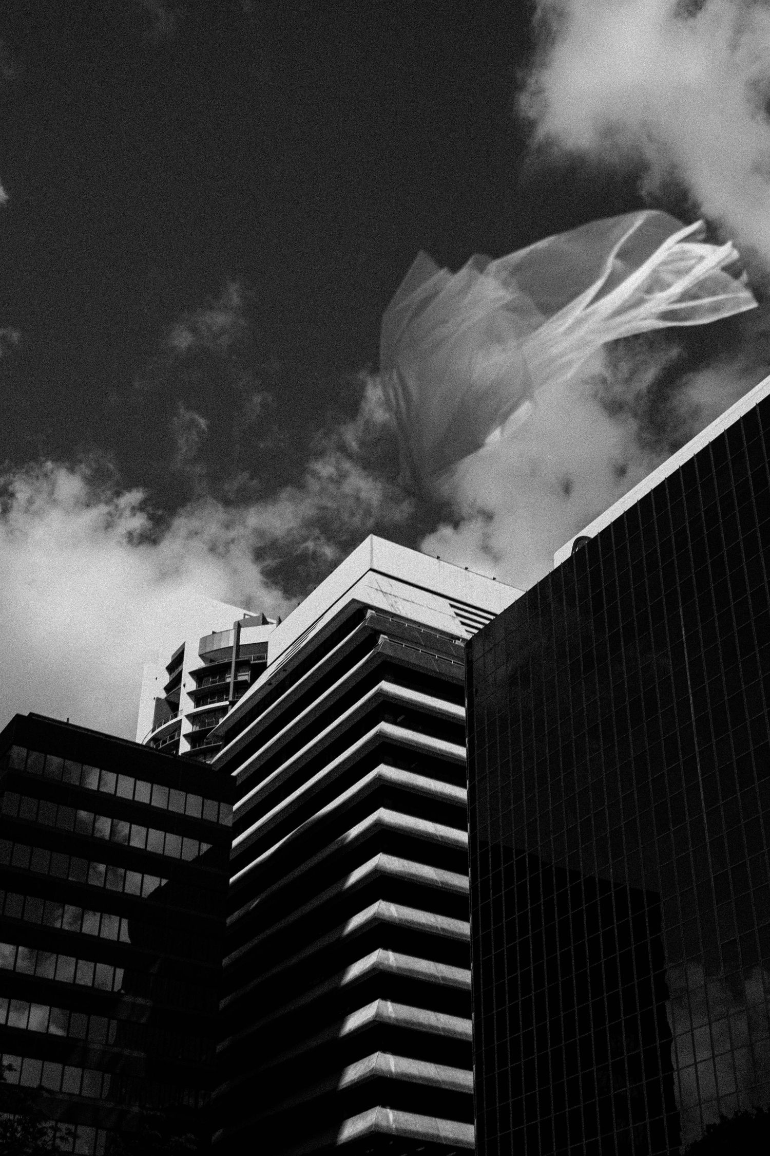 Black and white architectural photo of modern office buildings with dramatic clouds and geometric patterns in low angle view.