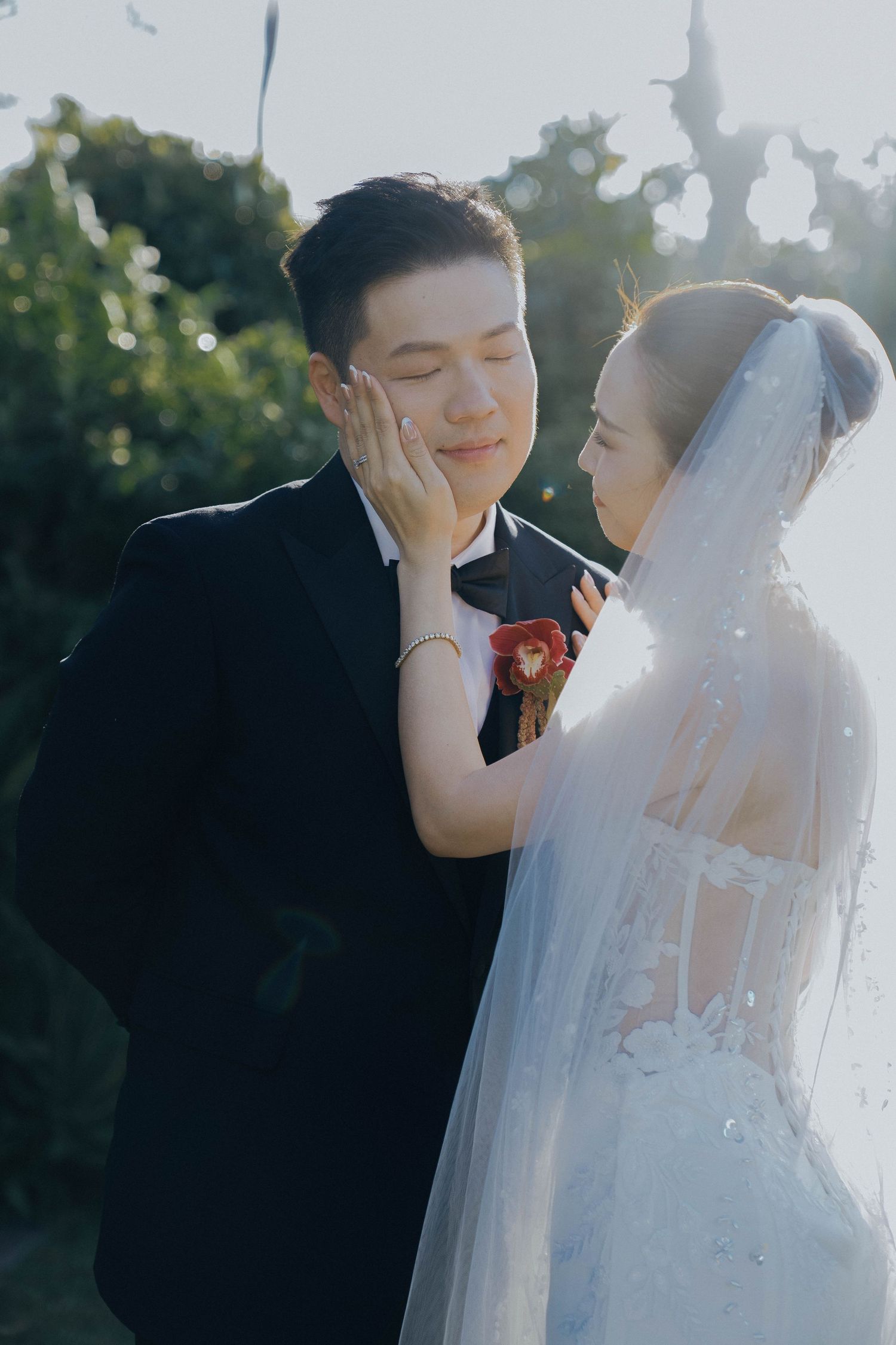 A romantic wedding photoshoot outdoors with a couple in traditional white dress and black tuxedo sharing tender moments.