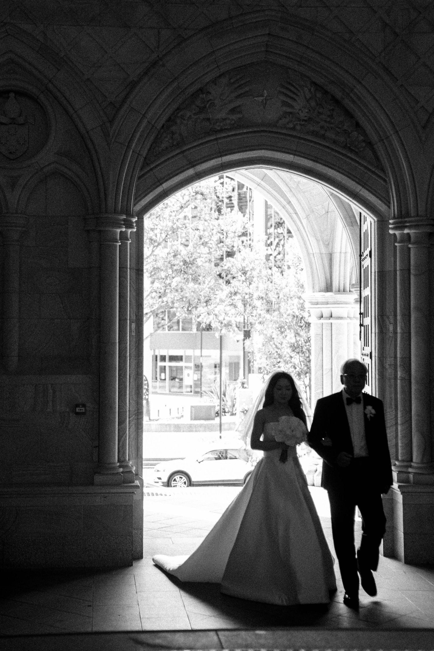 Silhouetted couple stands in arched doorway with bright outdoor light creating dramatic contrast in black and white photo.
