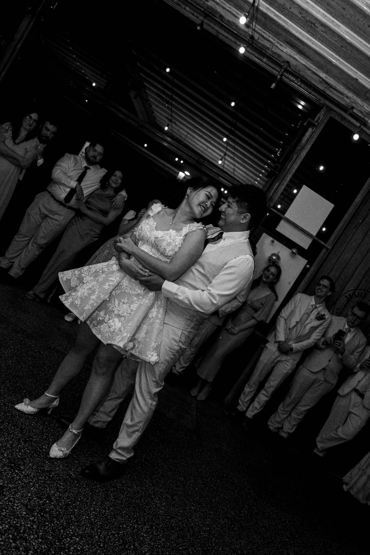Couples dancing together at a dimly lit wedding reception venue with dark carpeted floors.