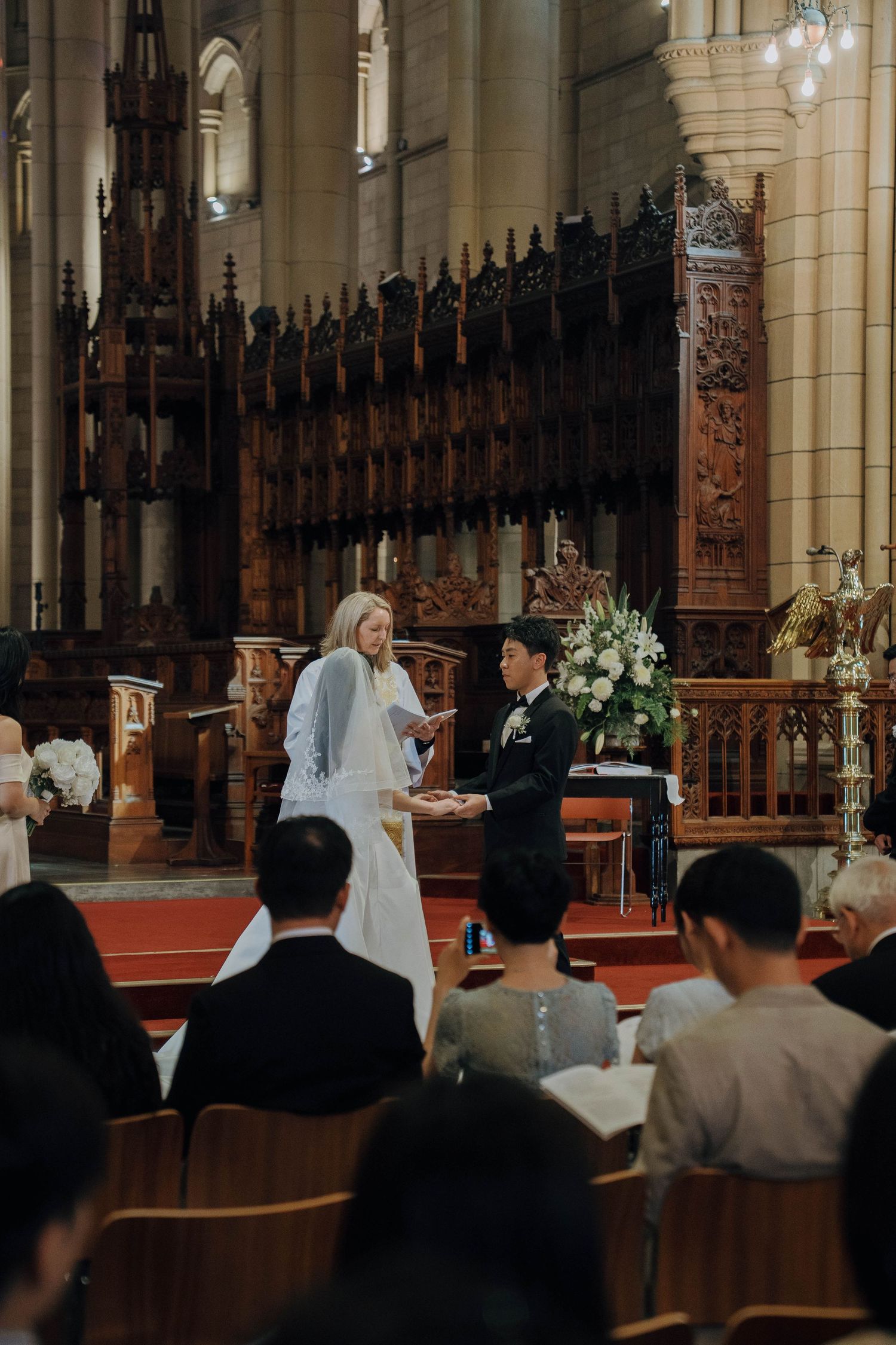 A wedding ceremony taking place in a grand cathedral with ornate wooden details and stained glass windows.