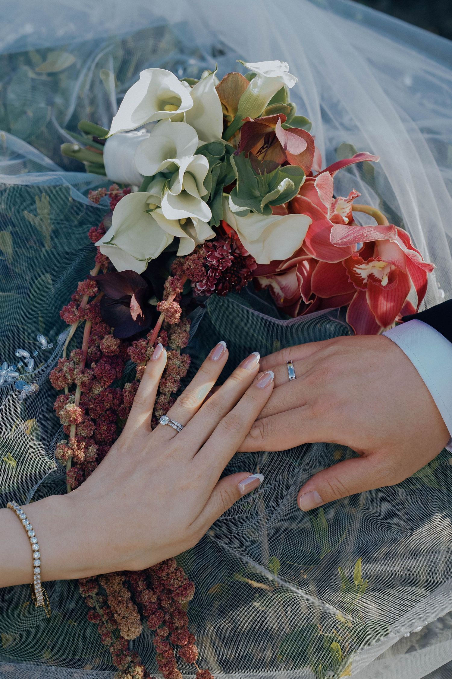 Close-up series of hands with rings and bracelets holding a romantic bridal bouquet with white and coral flowers.