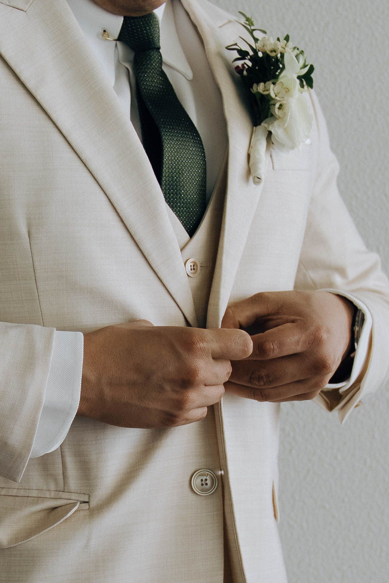 Close-up details of a cream colored suit jacket with boutonniere showing buttons and fabric texture.