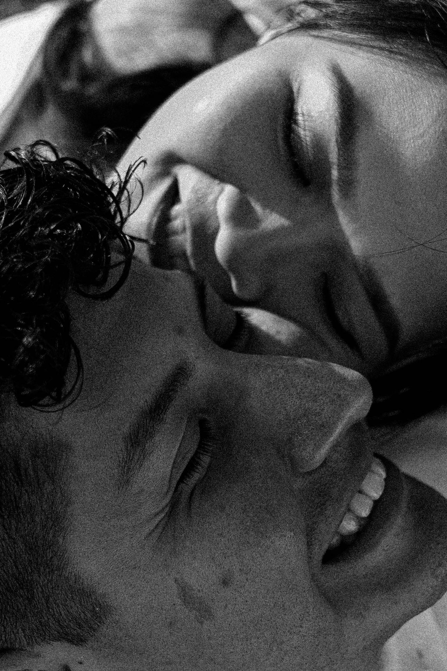 A black and white artistic photograph shows an intimate close-up moment between two people in shadow.