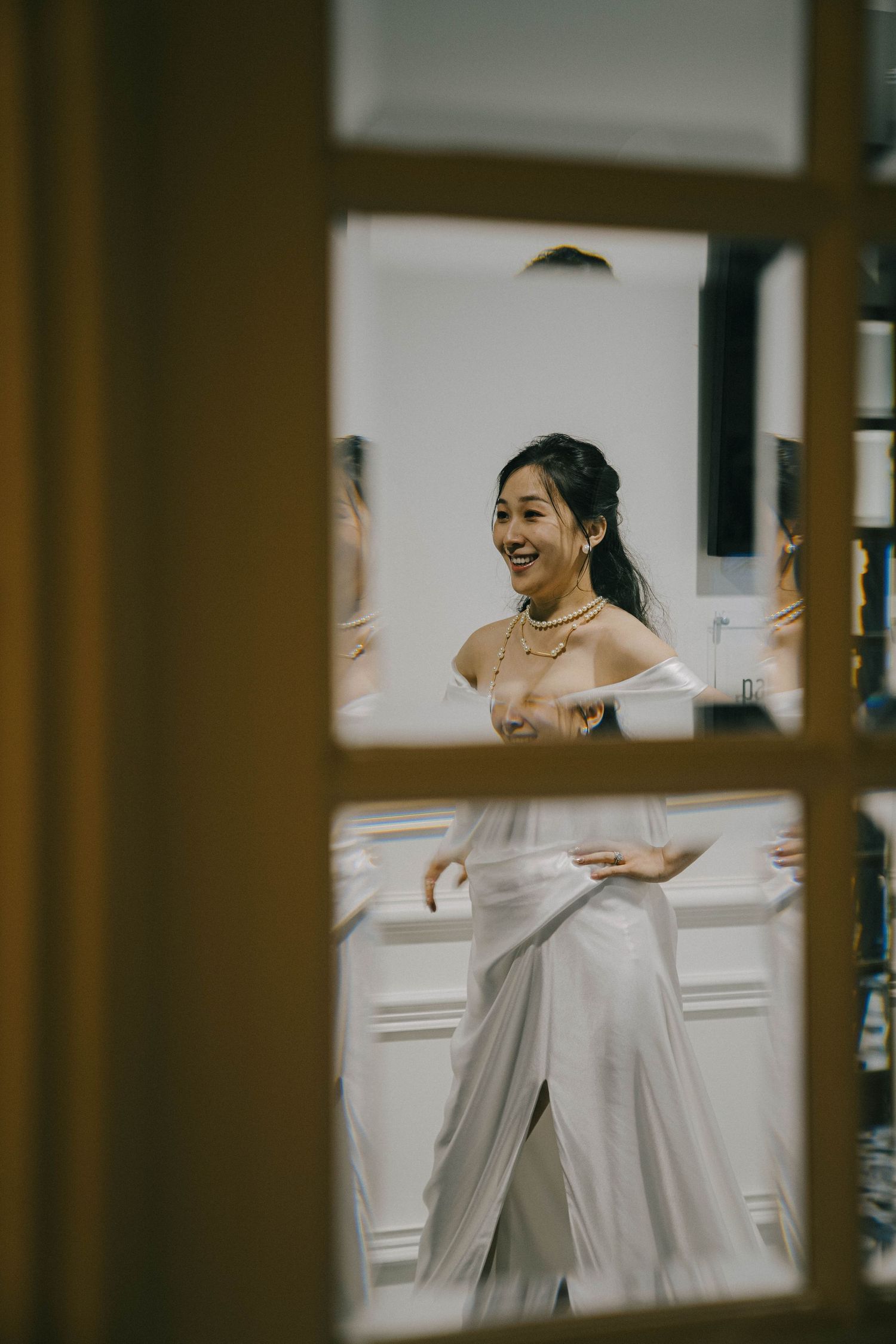 Through a doorframe, a joyful moment is captured as someone in an elegant white dress spins and laughs in a bright room.