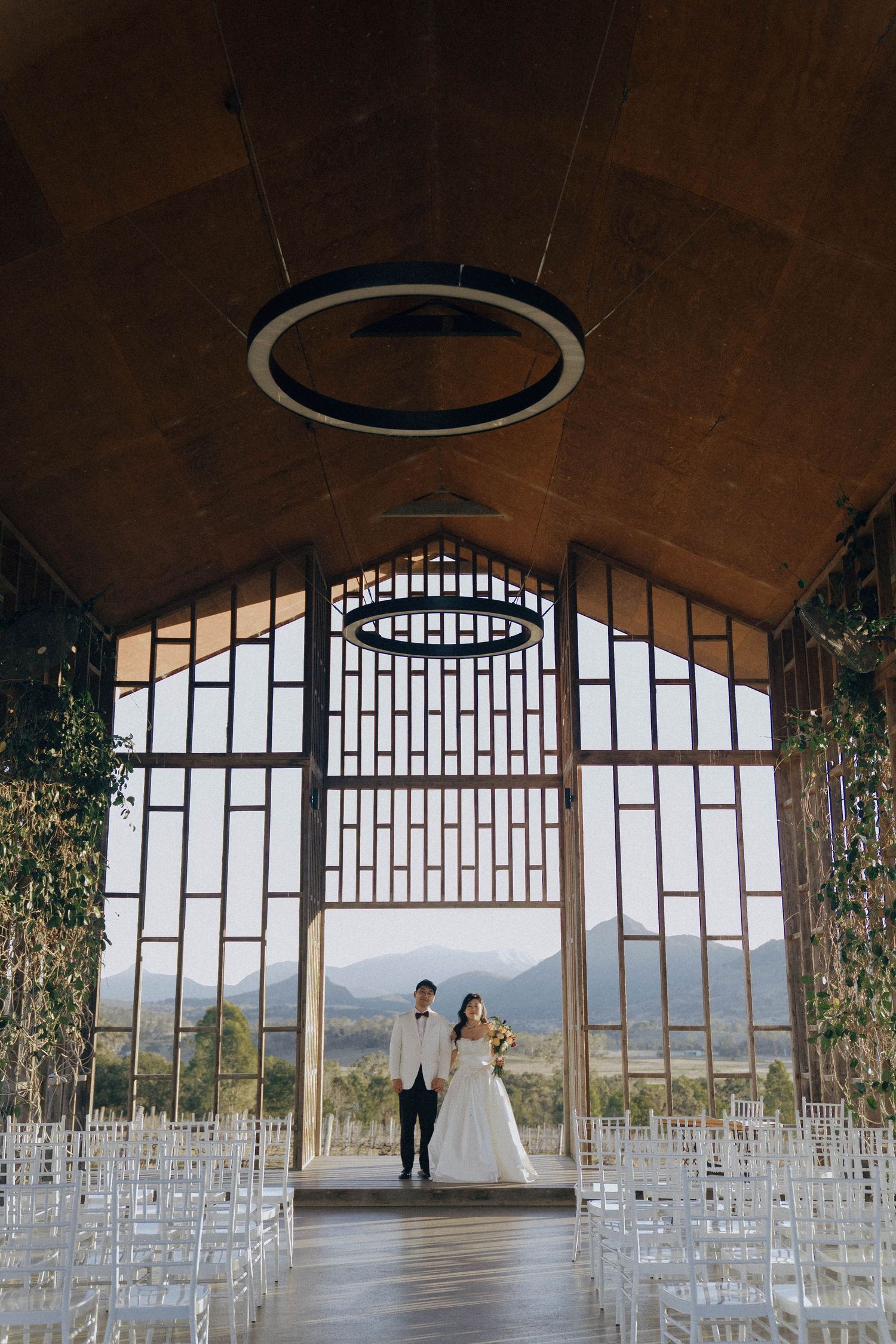 Panoramic view of a modern wedding venue with glass walls, mountain vistas, and rows of white chairs set up for ceremony.