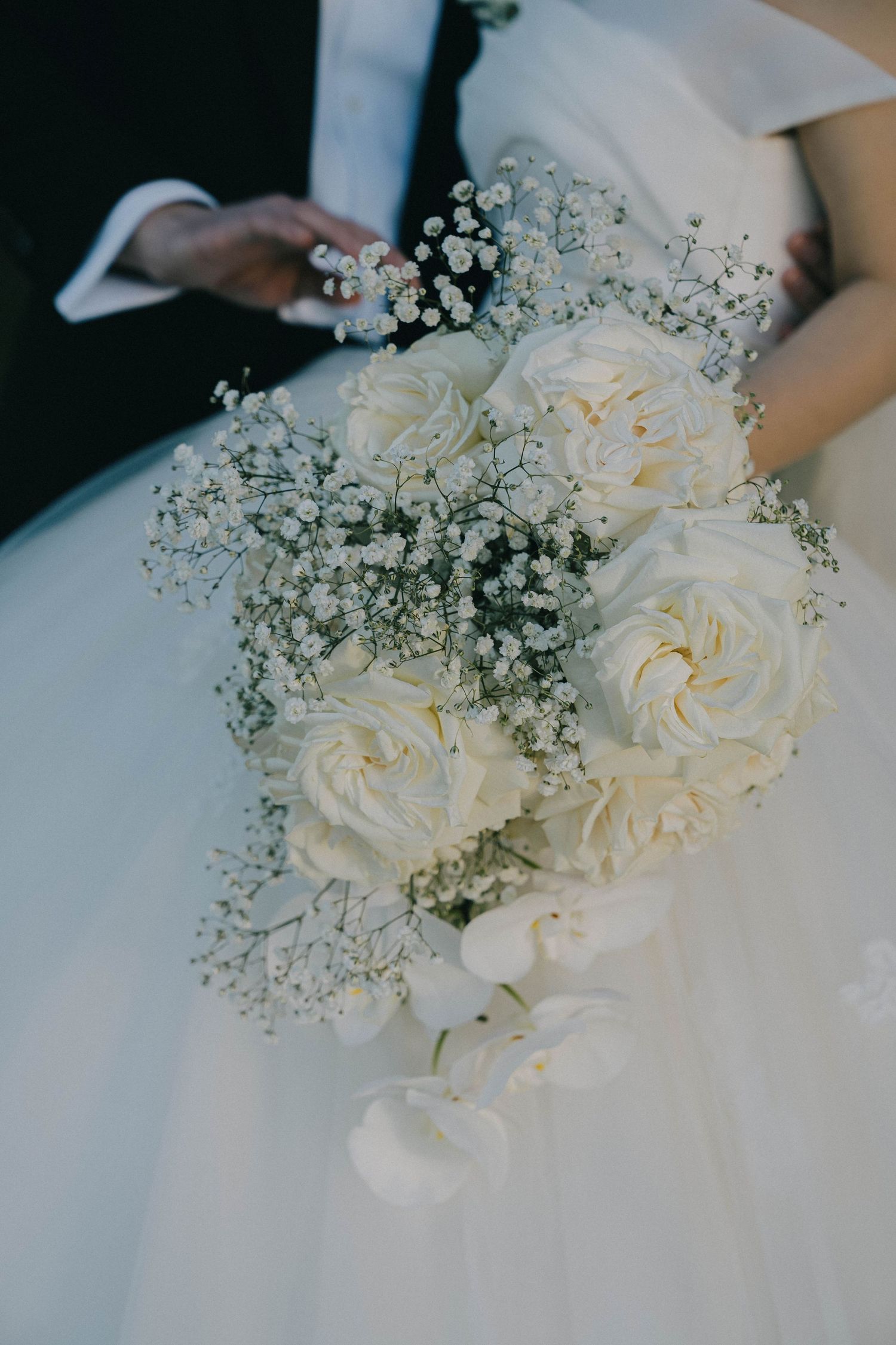 A delicate bridal bouquet featuring white roses and baby's breath against a white wedding dress background.