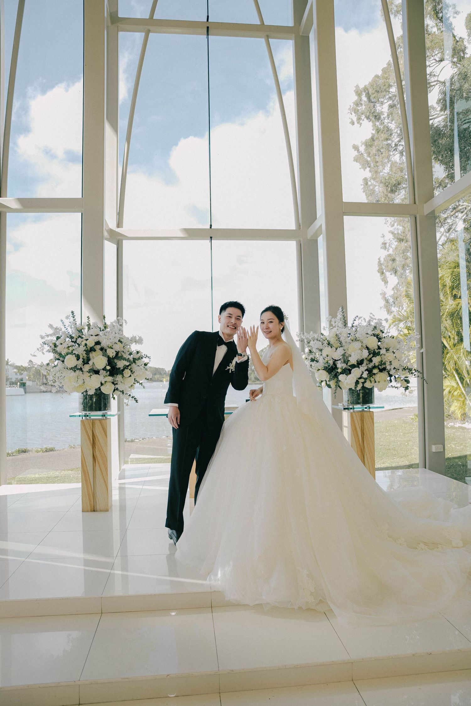 A romantic wedding photoshoot in a bright glass chapel with white floral decorations and natural sunlight streaming in.