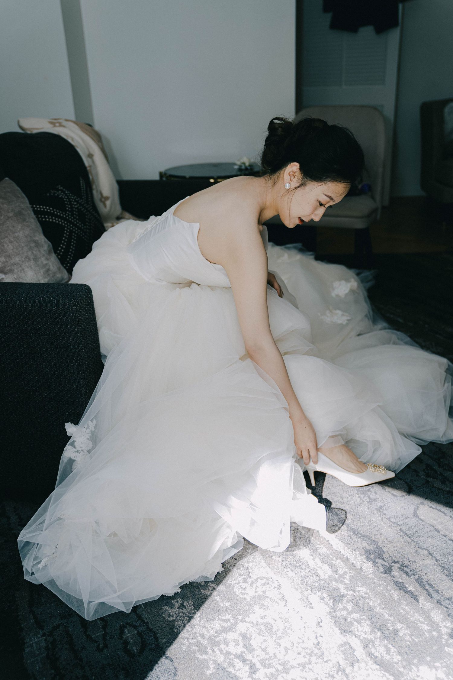 A figure in a flowing white tulle dress reclines gracefully across a bed in a dimly lit room.