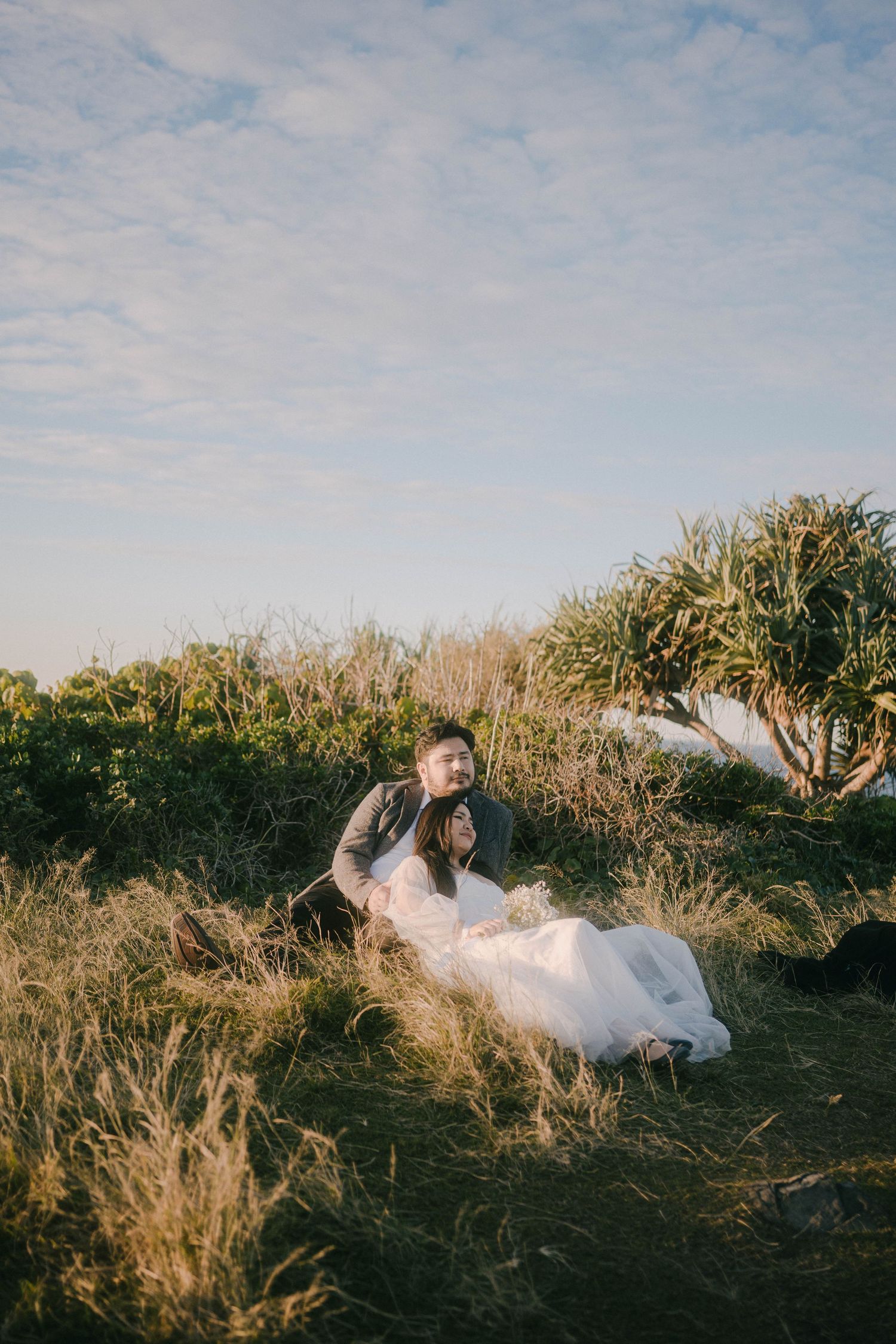 A person in a flowing white dress lies in tall grass at sunset creating a dreamy outdoor portrait series.