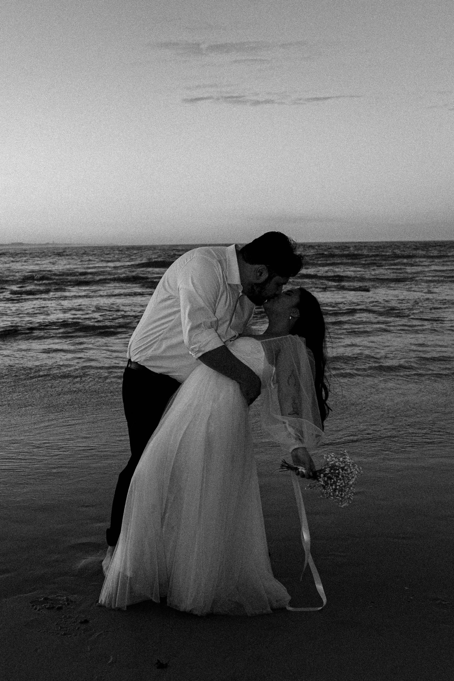 A romantic black and white beach wedding photo sequence showing a couple embracing by the ocean at sunset.