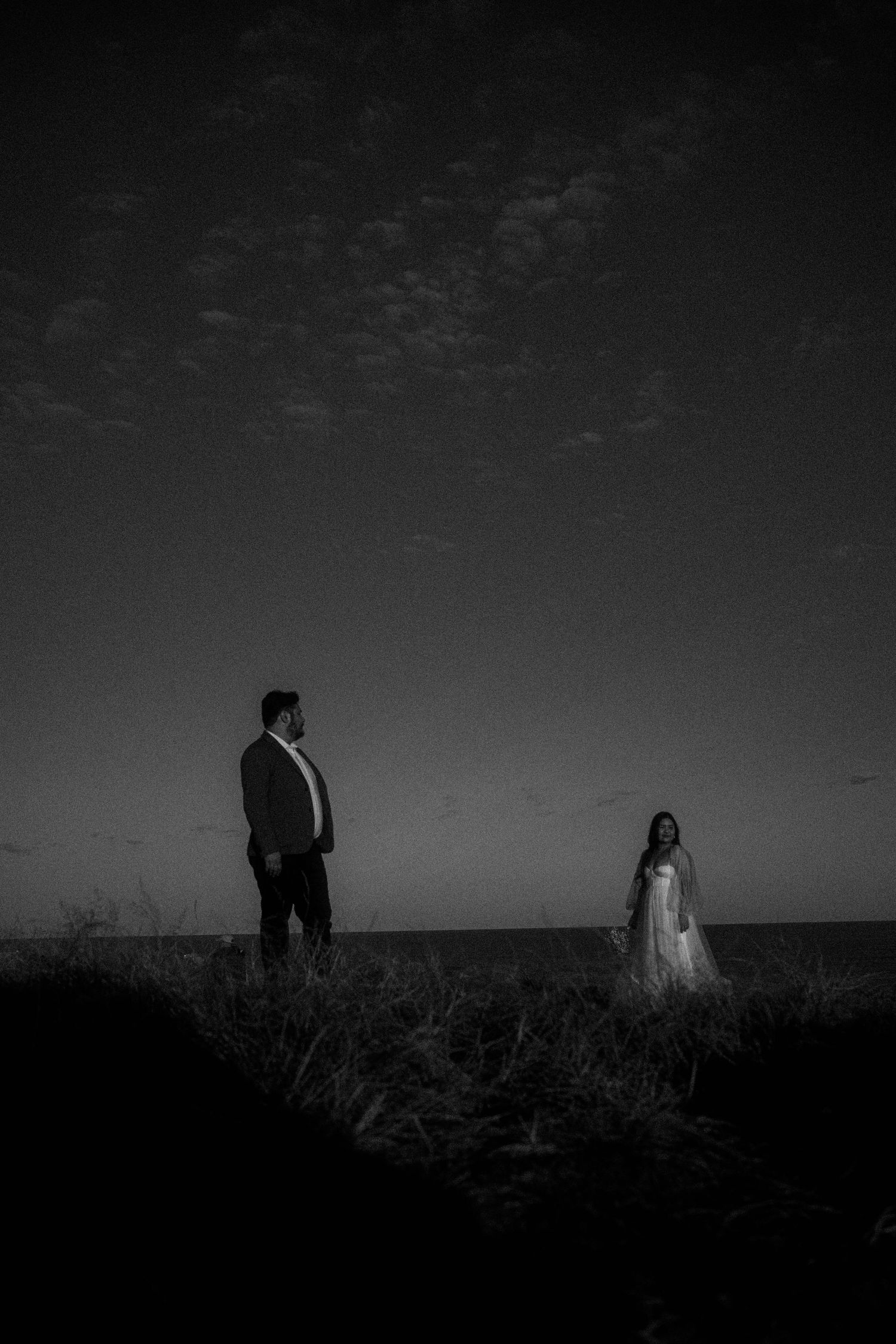 A dramatic black and white panoramic series showing silhouettes of a couple against a moody sky in a field.