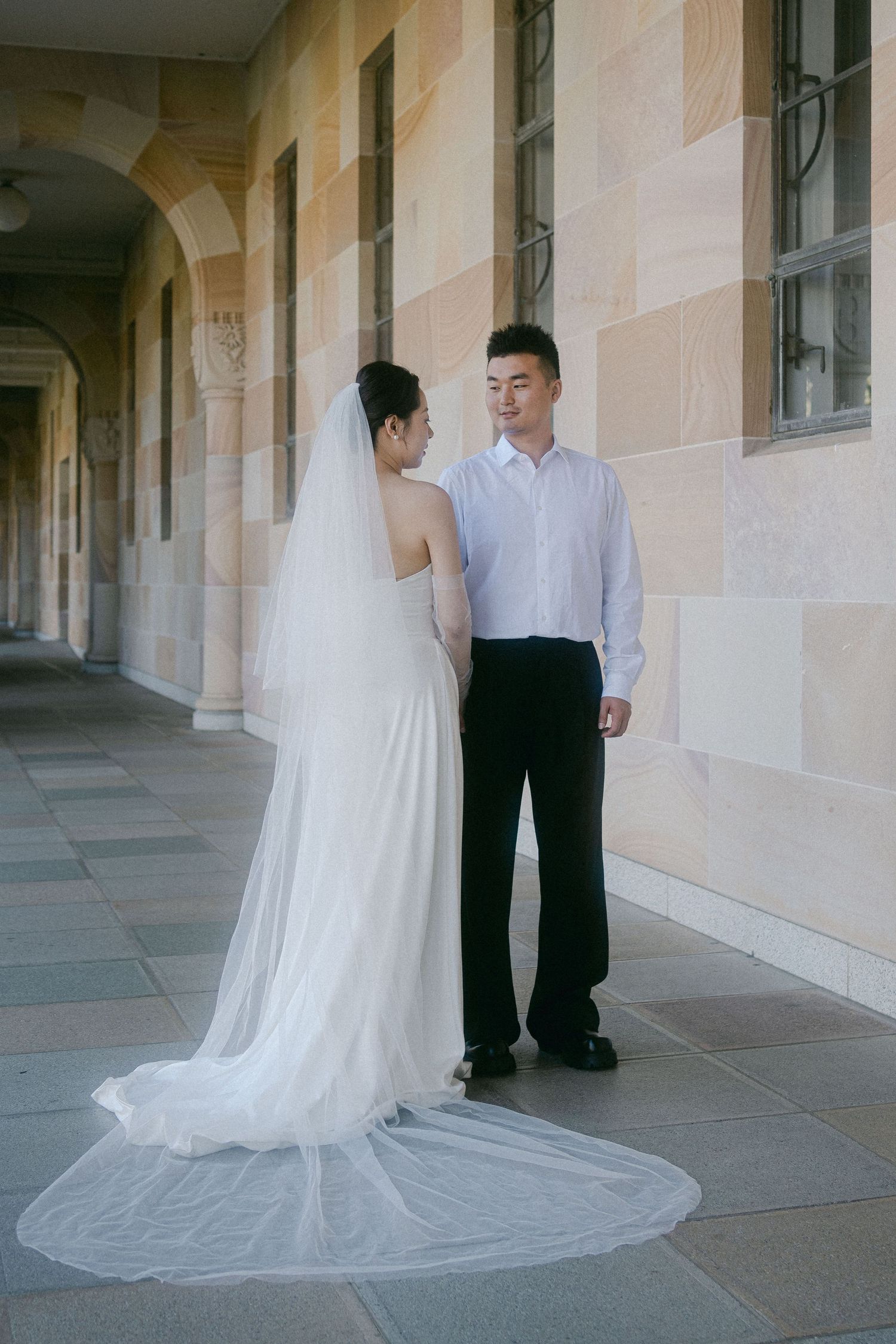 A romantic wedding couple standing in an elegant archway corridor with the bride's flowing white train on display.