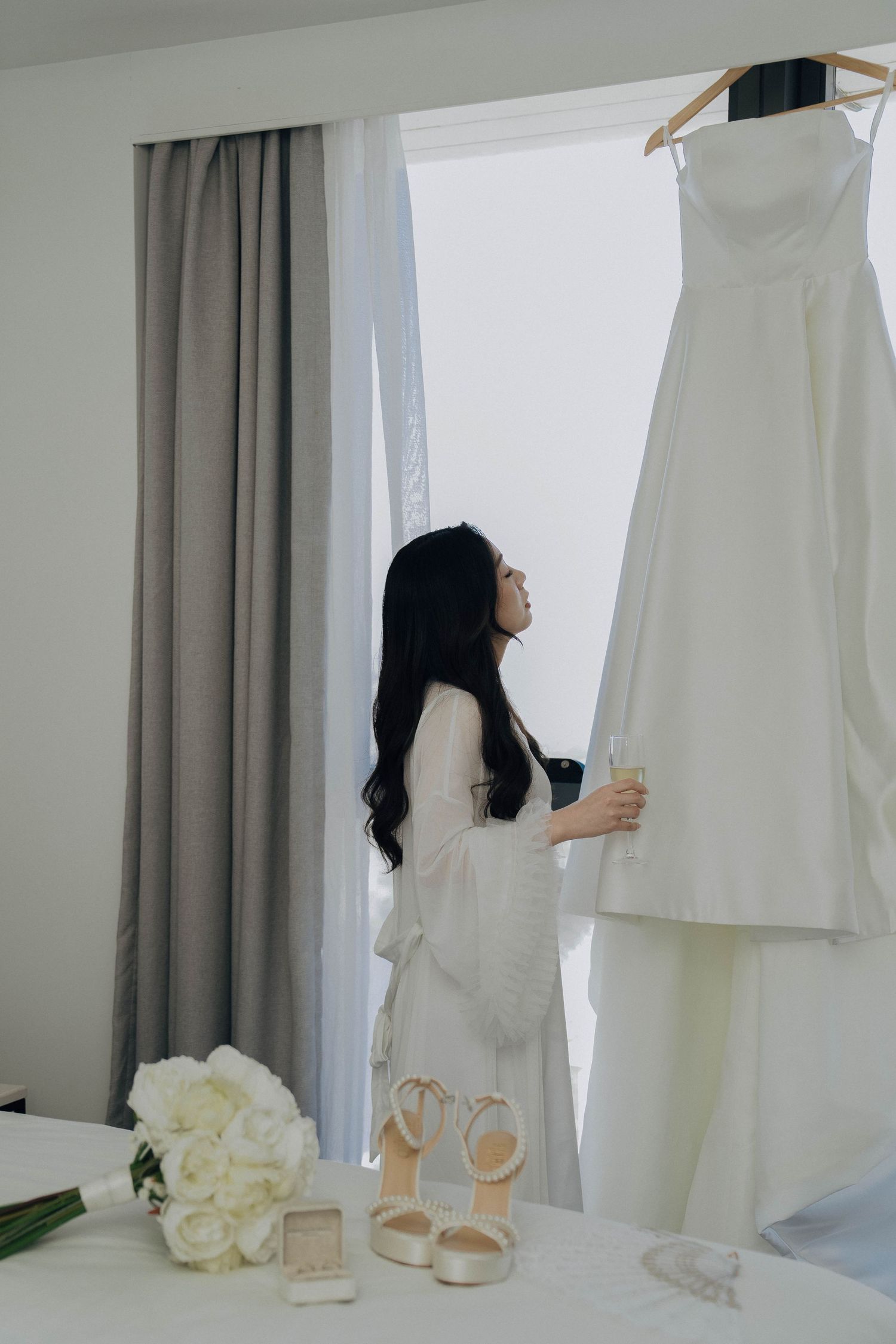 A minimalist scene shows a woman in white preparing for a wedding with shoes, flowers and gowns displayed.