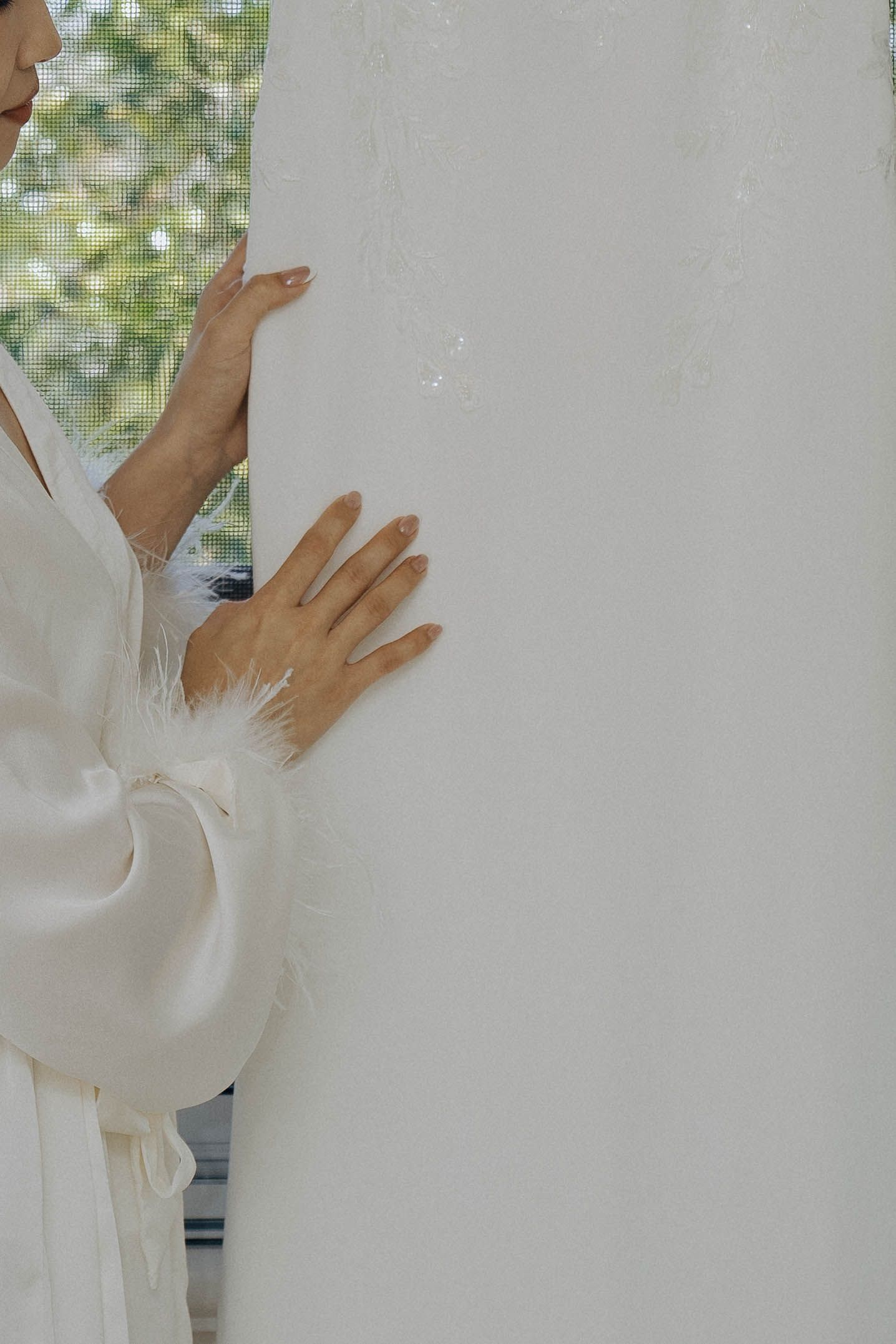 Hands in white sleeves gently touch a white wall surface in soft natural lighting.