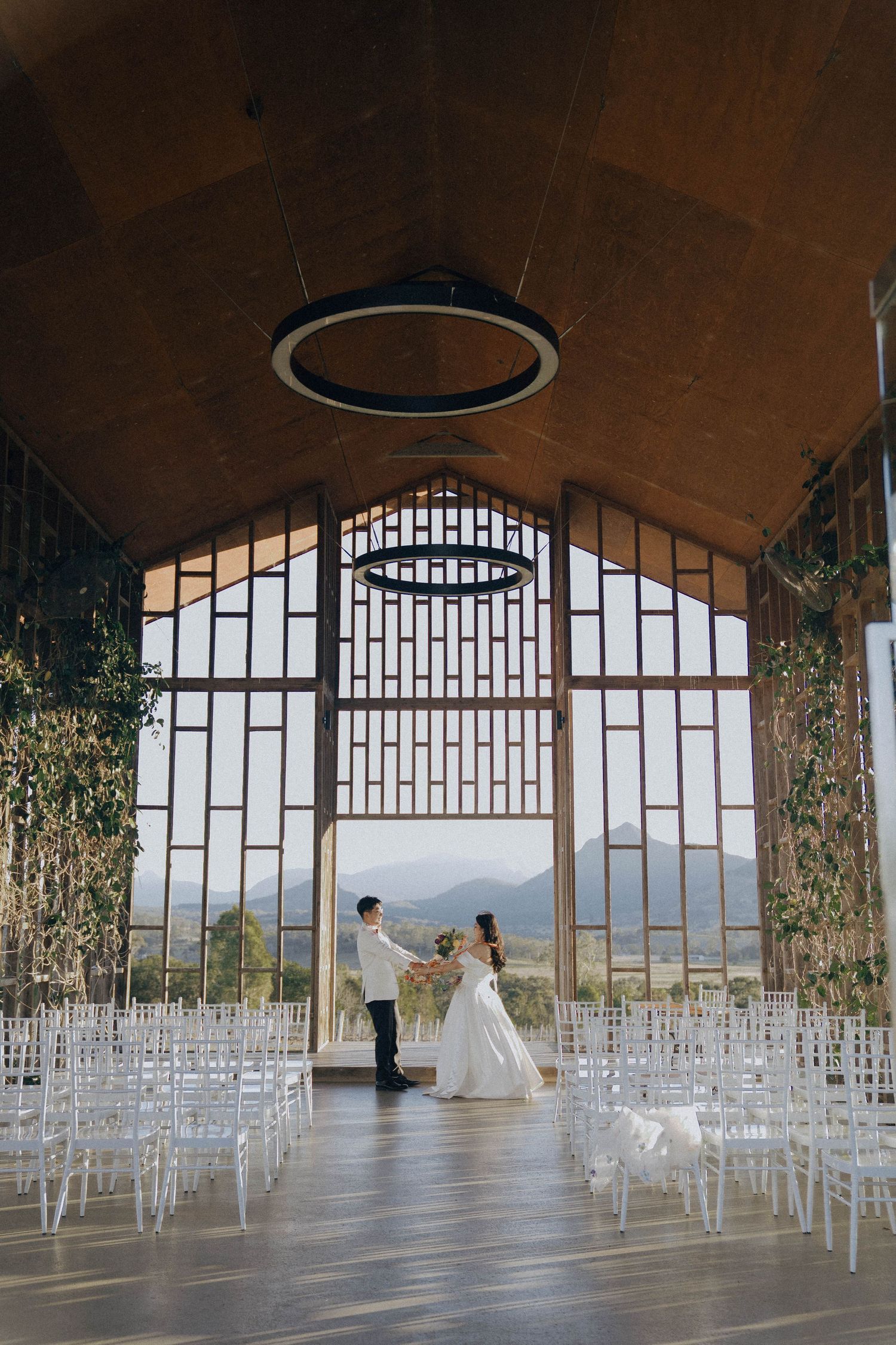 Modern chapel with glass walls showcases panoramic mountain views and rows of white chairs set for a wedding ceremony.