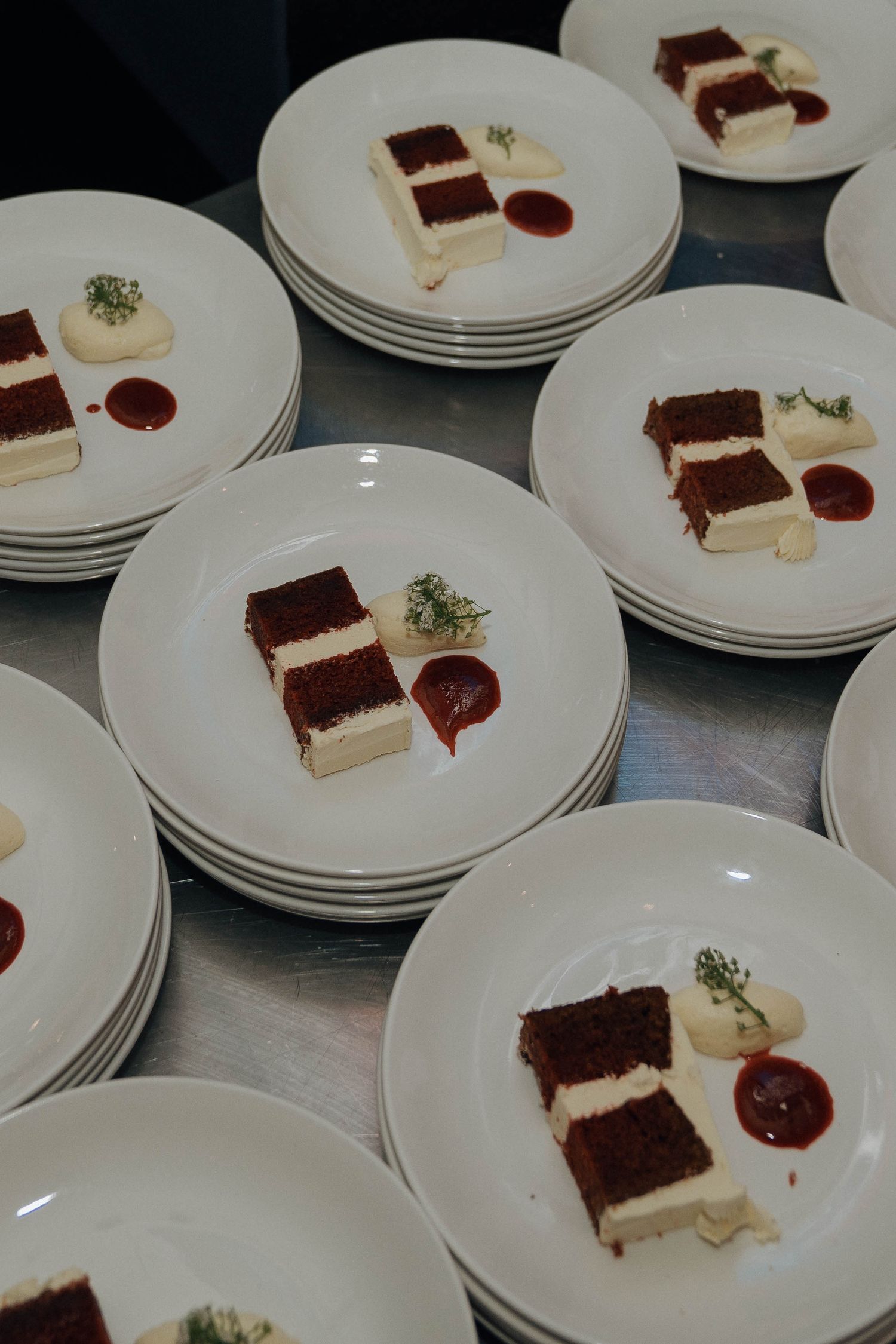 Multiple white plates arranged in rows displaying identical dessert portions with chocolate cake and cream components.