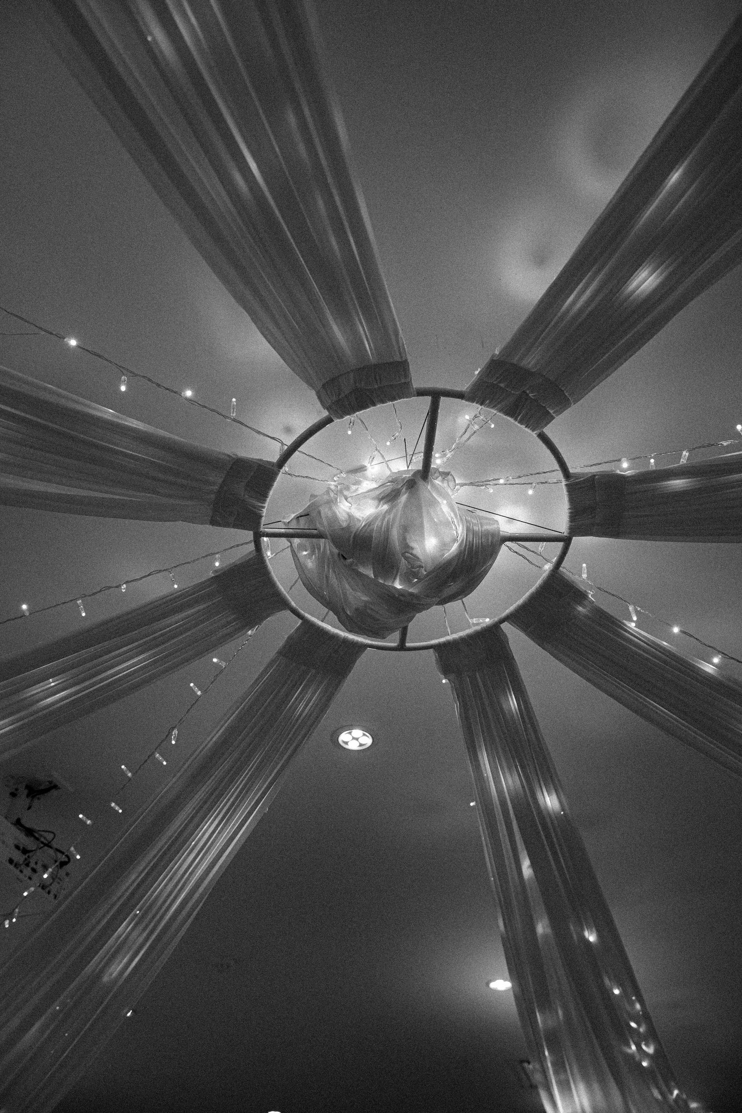 Black and white architectural abstract showing a circular ceiling pattern with radiating beams and hanging lights.