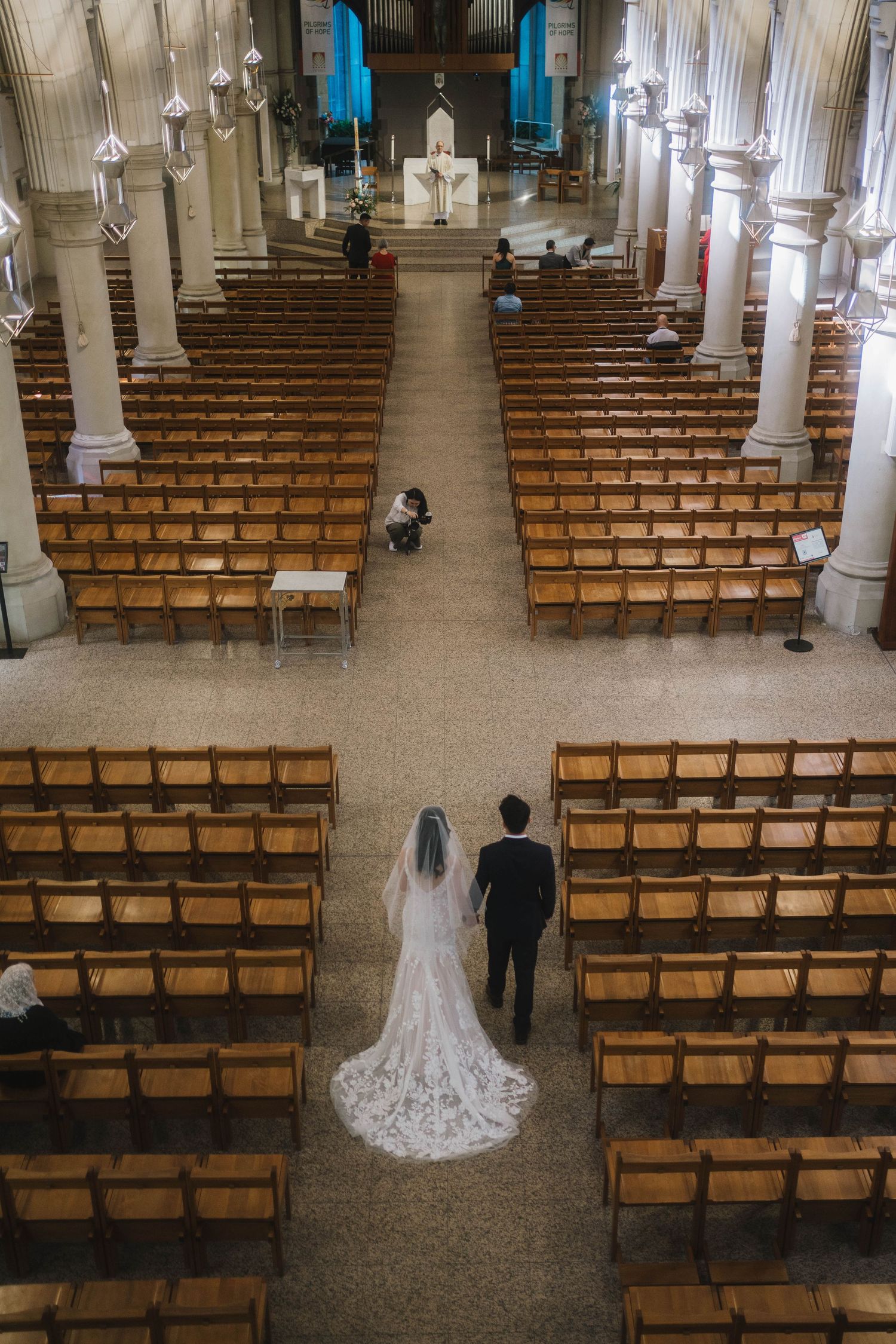 Overhead view of a large church interior with wooden pews and ornate pillars during an intimate wedding ceremony.