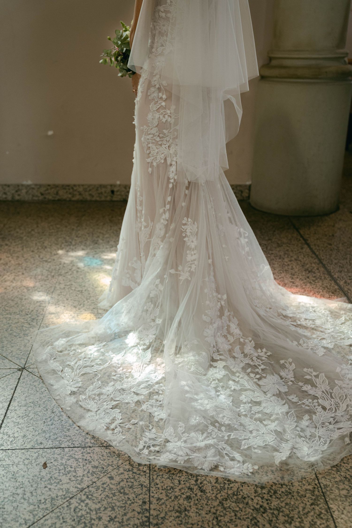 Beautiful lace wedding gown with long flowing train showcasing intricate floral embroidery details on cathedral-length veil.