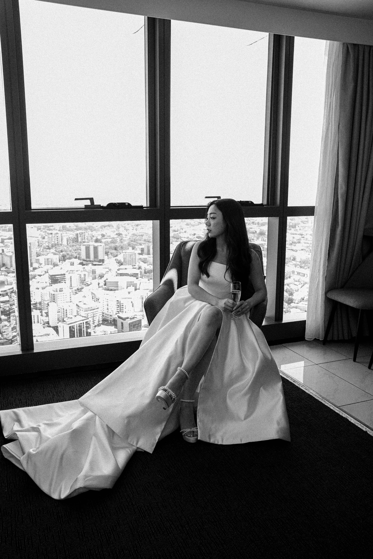 A black and white panoramic sequence of a figure in white fabric reclining against windows overlooking a cityscape.