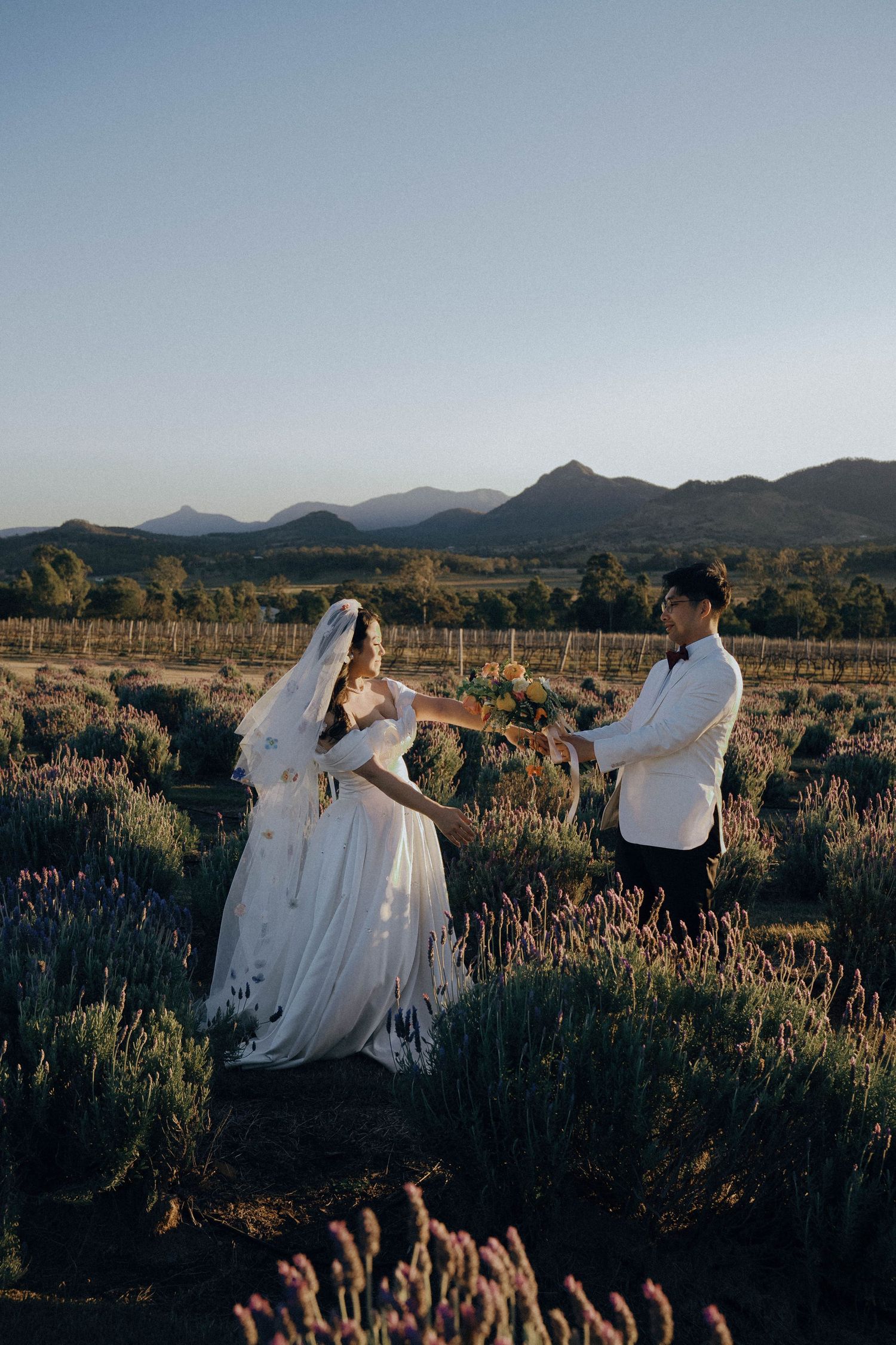 Couple dancing in a desert field at sunset with mountains in the background and purple wildflowers in the foreground.