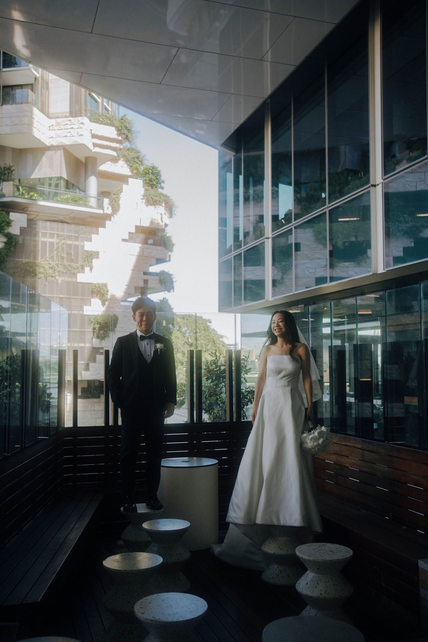 A couple stands in silhouette against glass windows in a modern building interior, creating a dramatic architectural scene.