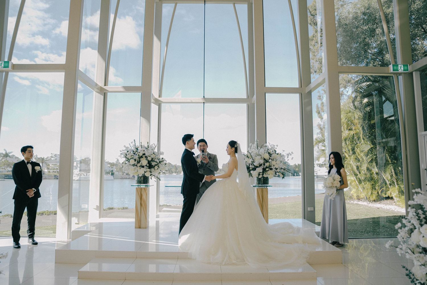 A panoramic view of a modern glass-walled wedding venue with white curtains and floral decorations by the windows.