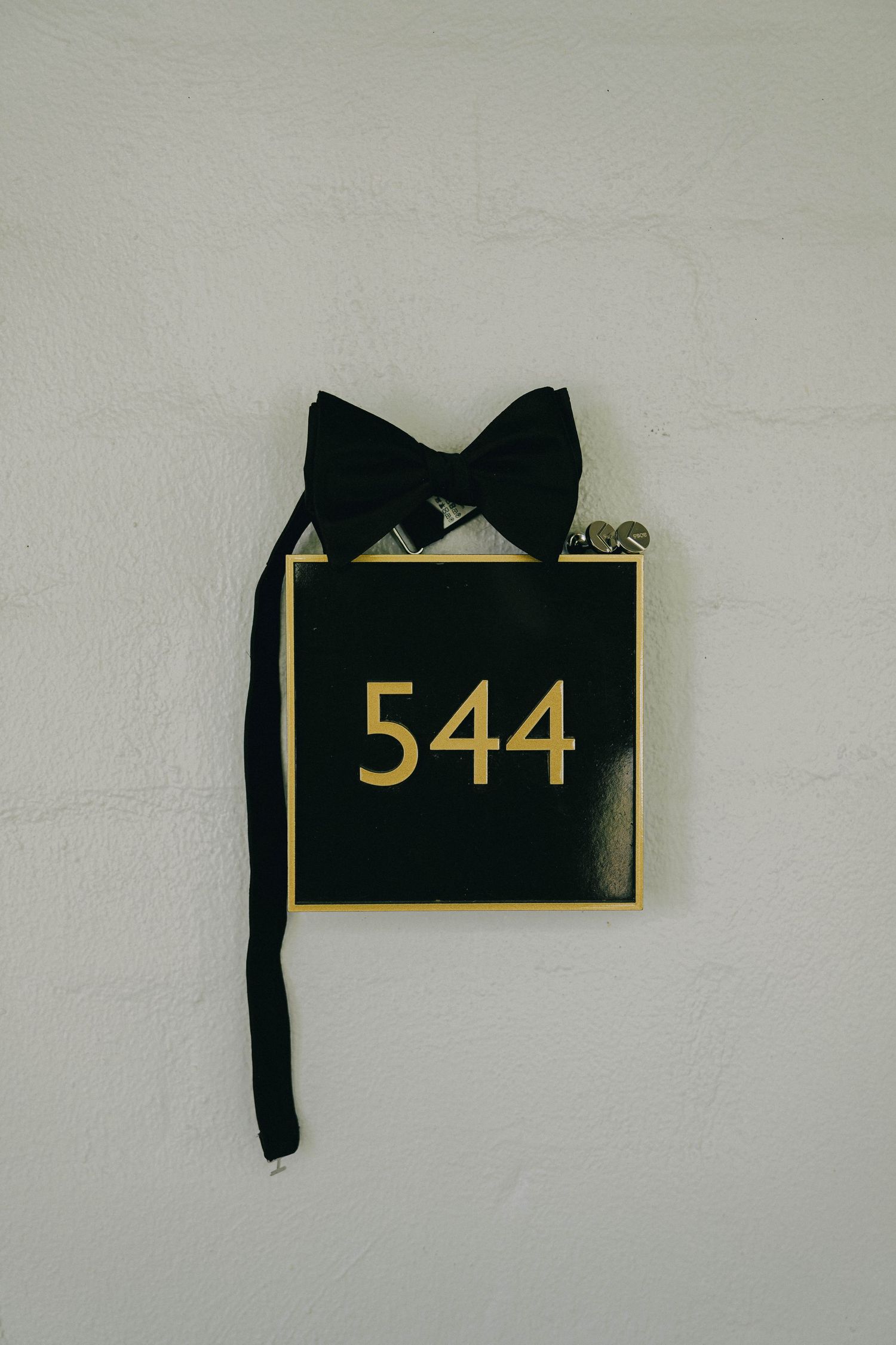 A sequence of torn black paper pieces with gold numbers 544 and text fragments against a white wall.